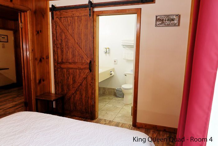 Bedroom with open wooden door leading to a small bathroom, white bedspread in foreground, pink curtain at right