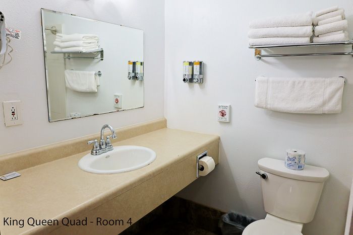 Small hotel bathroom with sink, mirror, toilet, and neatly folded towels.