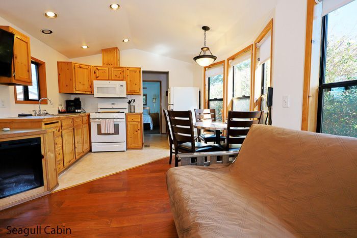 Bright cabin kitchen and dining area with wood cabinets, white appliances, and large windows