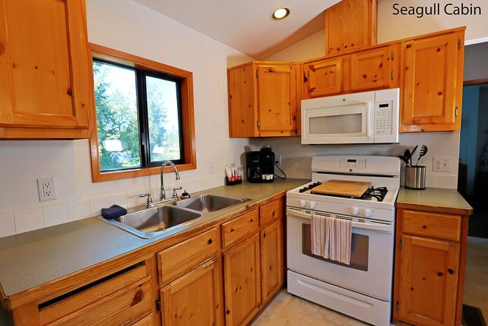 Wooden cabin kitchen with white appliances, sink by window, and granite counters