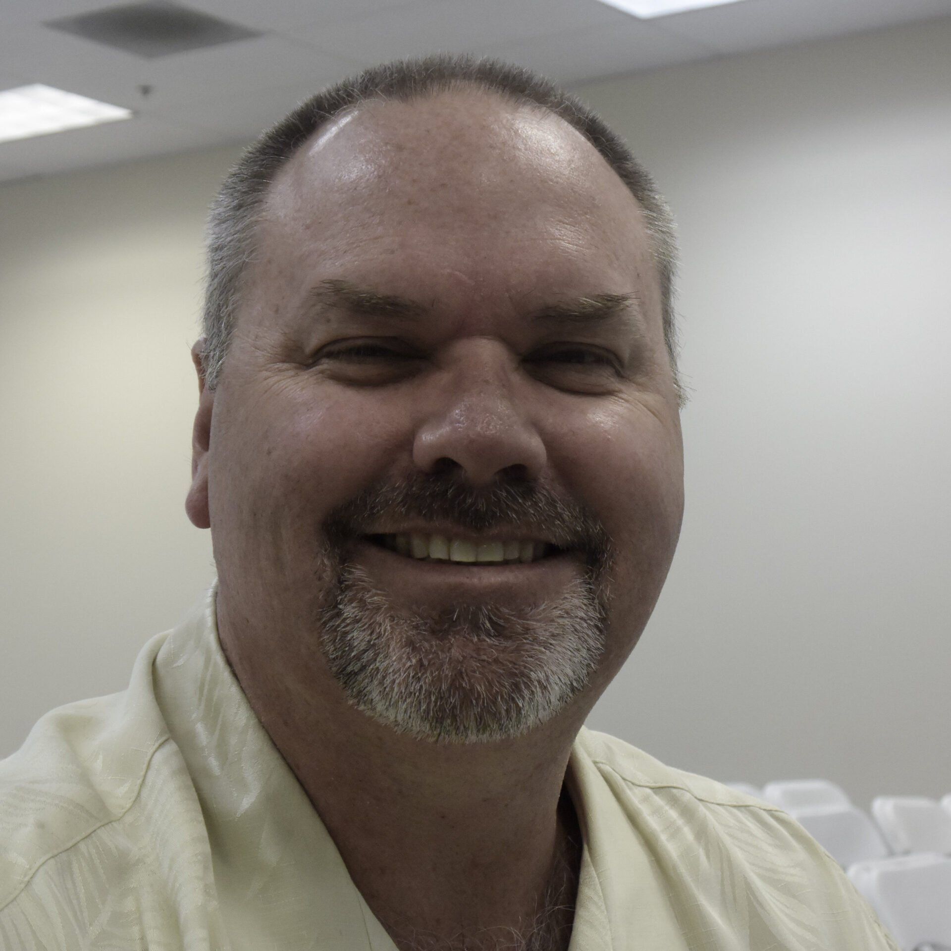 Clancy Fort with a goatee in a beige shirt, standing in a bright conference room.
