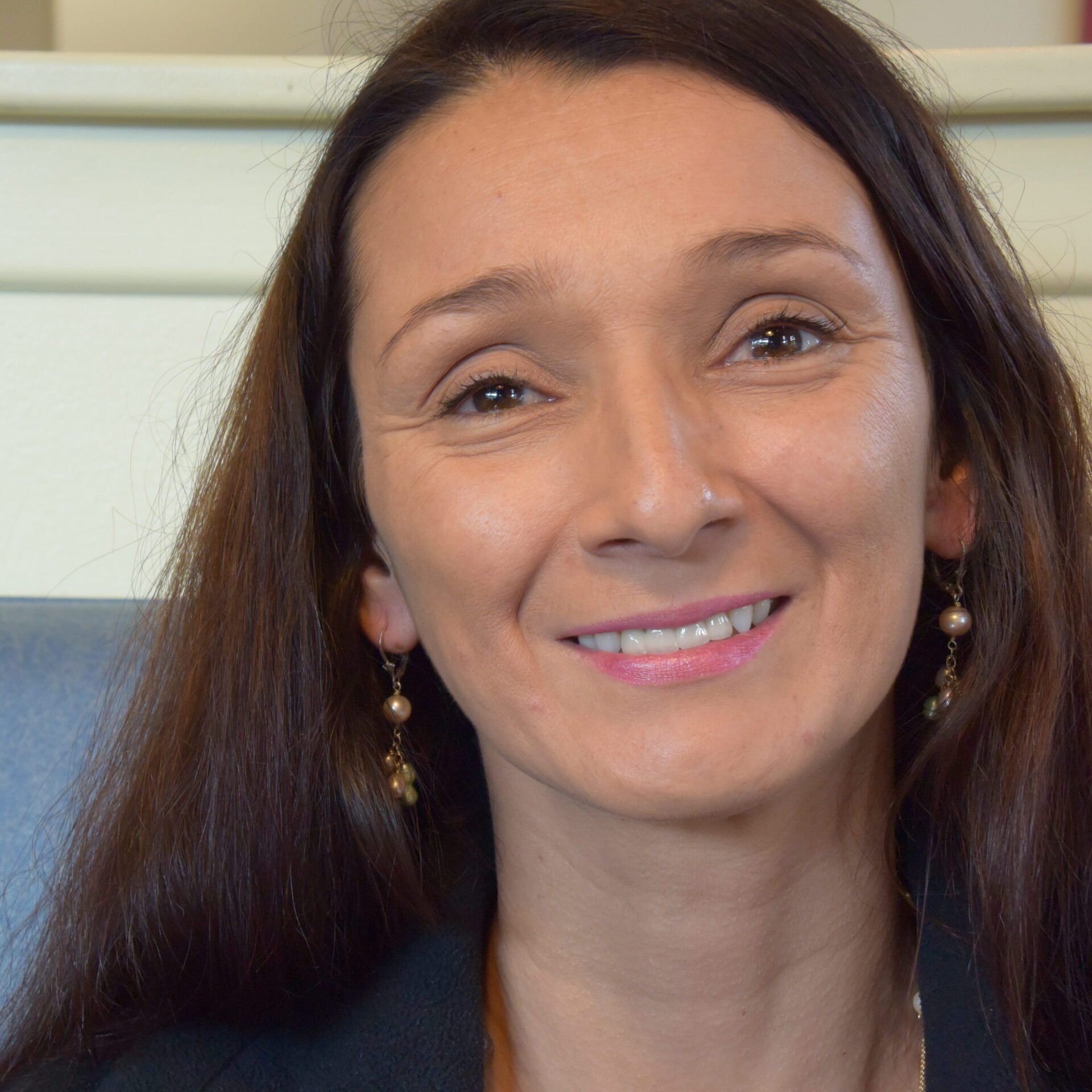 Celina Fort with long dark hair and earrings, seated indoors against a light background