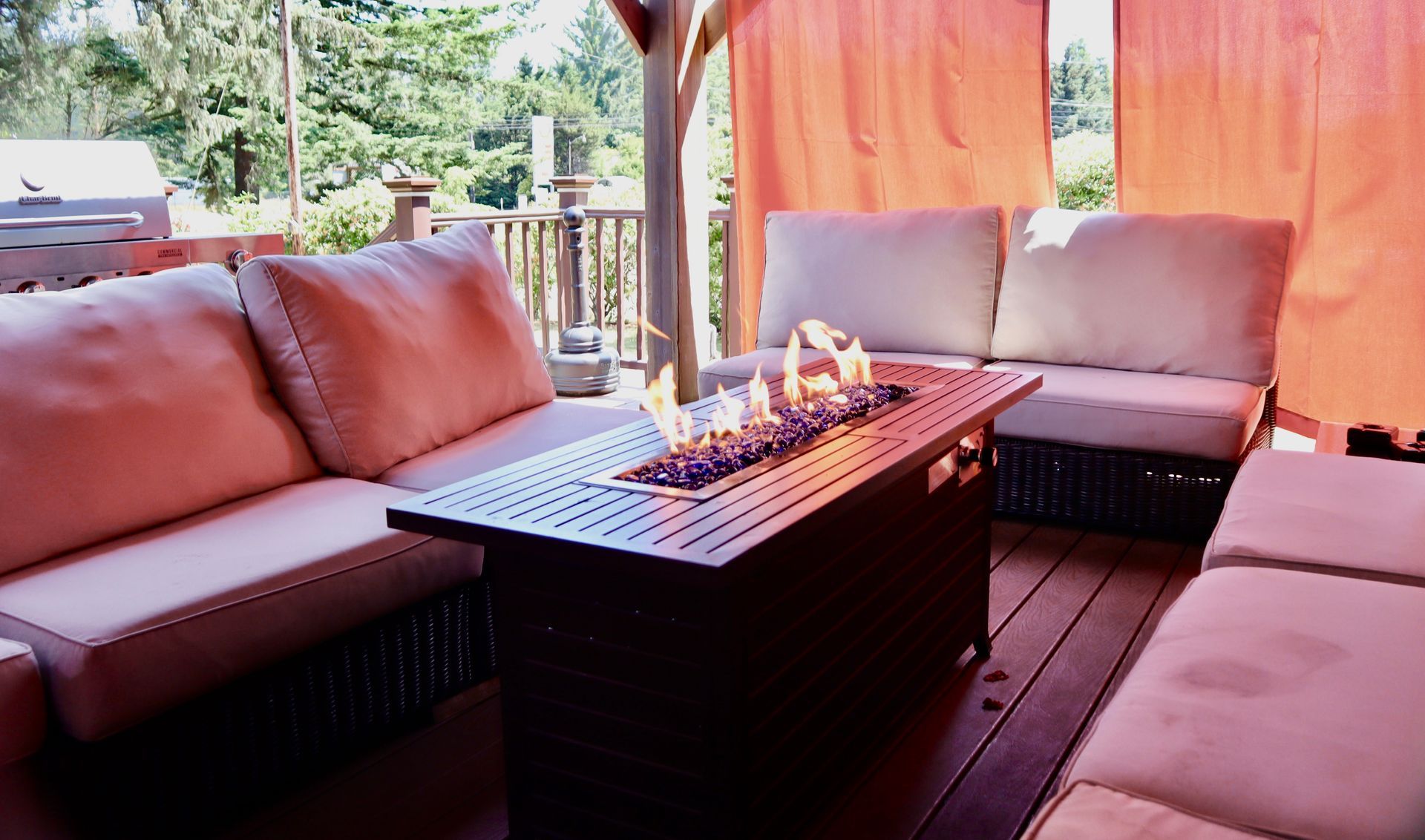 Patio seating area with cushioned sofas around a fire table, lit by warm orange curtains.
