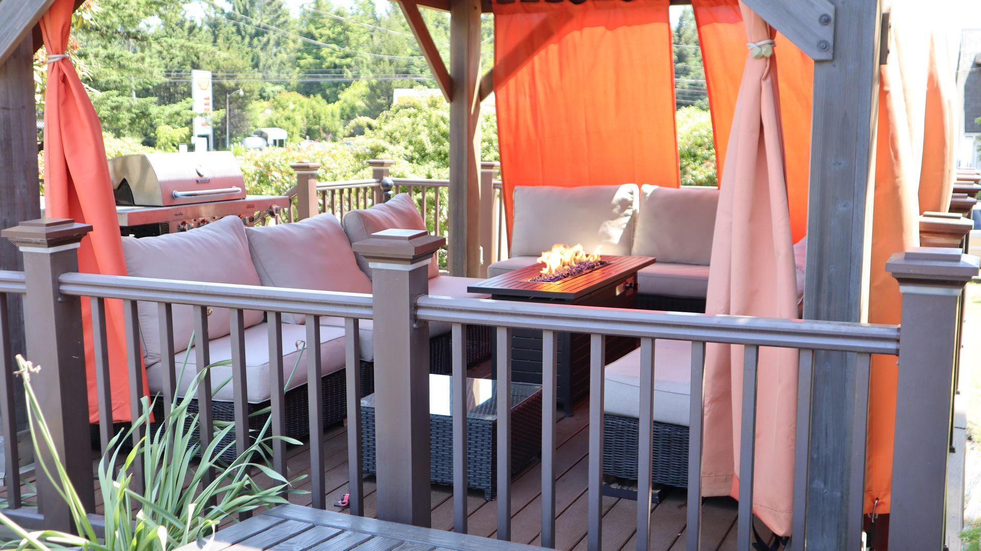 Outdoor patio dining area with orange curtains, cushioned chairs, and a fire pit