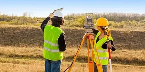 A man and a woman are working on a survey in a field.