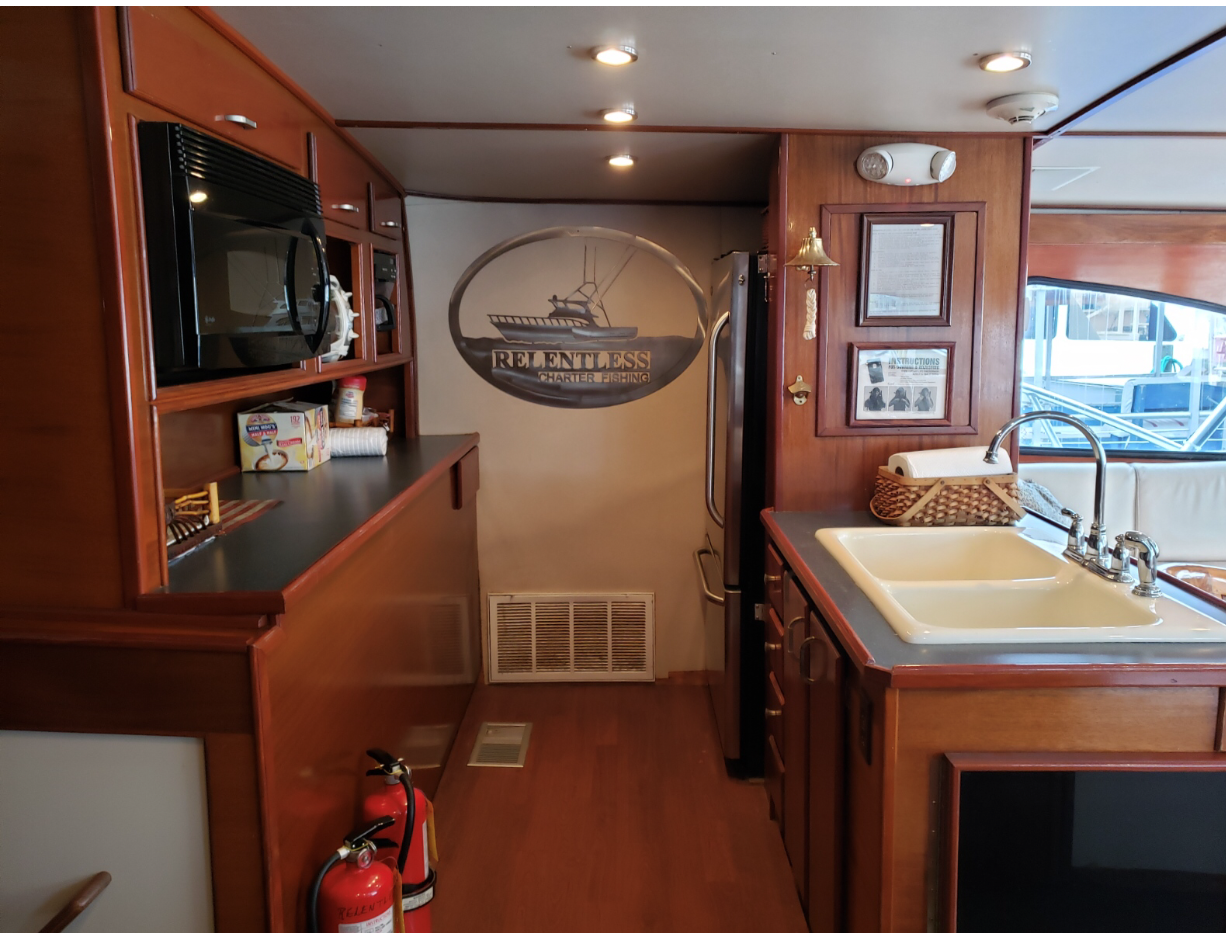 Fishing Destin, FL | Destin Harbor | Charter Boat Relentless | www.charterboatrelentless.com | A Luxury Charter Boat at Everyday Rates | 65' x 20' | A kitchen with a sink a microwave and a fire extinguisher.