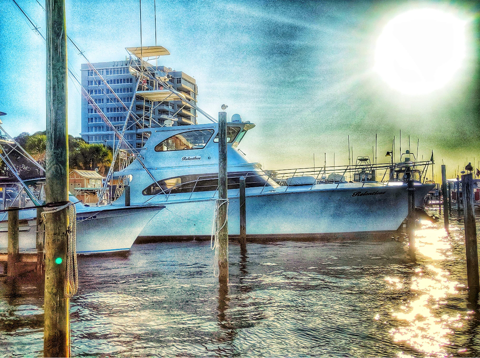 Fishing Destin, FL | Destin Harbor | Charter Boat Relentless | www.charterboatrelentless.com | A Luxury Charter Boat at Everyday Rates | 65' x 20' | A boat is slipped at a dock in Destin Harbor, with a condo in the background.