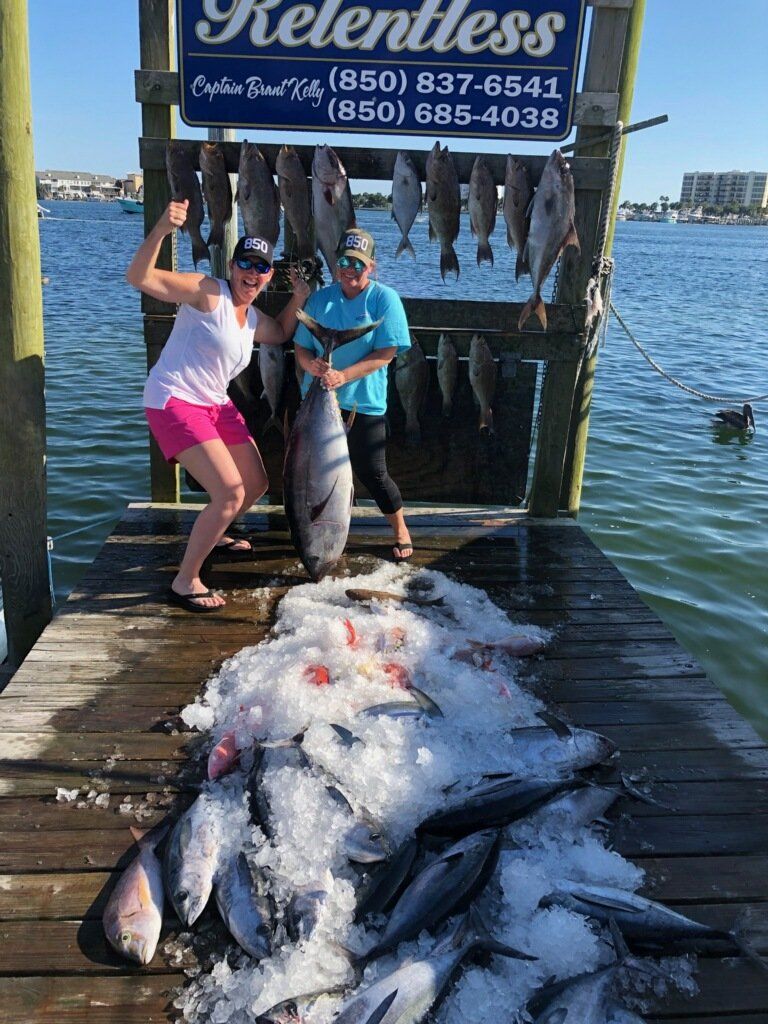 Two women are standing on a dock holding large fish.