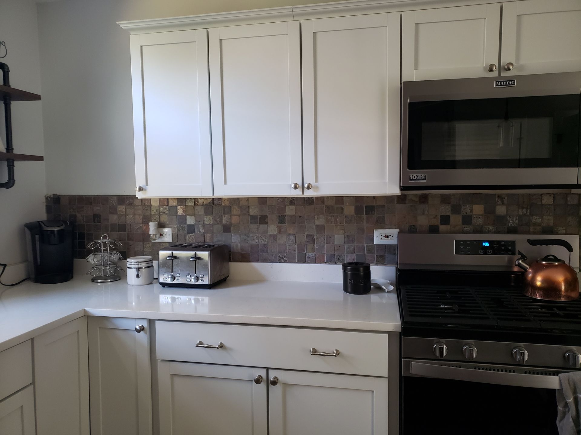 Modern kitchen with white cabinets, mosaic backsplash, microwave, stove, and countertop appliances