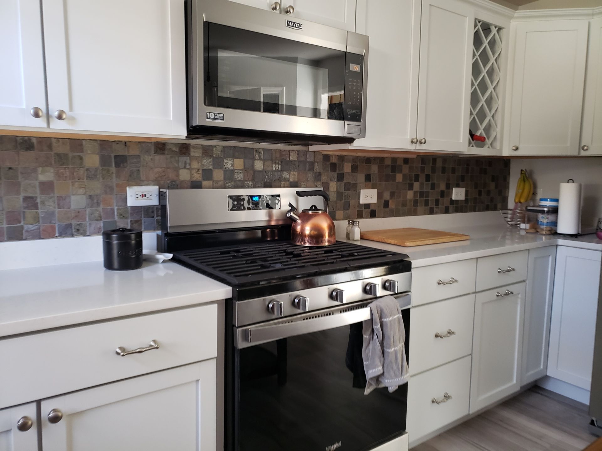 Modern white kitchen with stainless steel appliances, tiled backsplash, and a stove with copper pots on top
