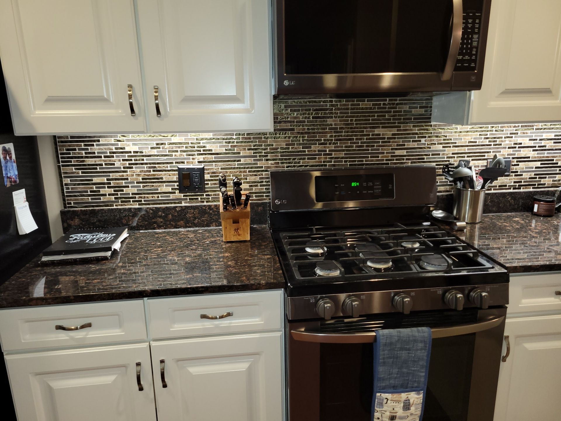 Kitchen with white cabinets, dark granite counters, stainless steel appliances, and a gas stove with a blue towel.