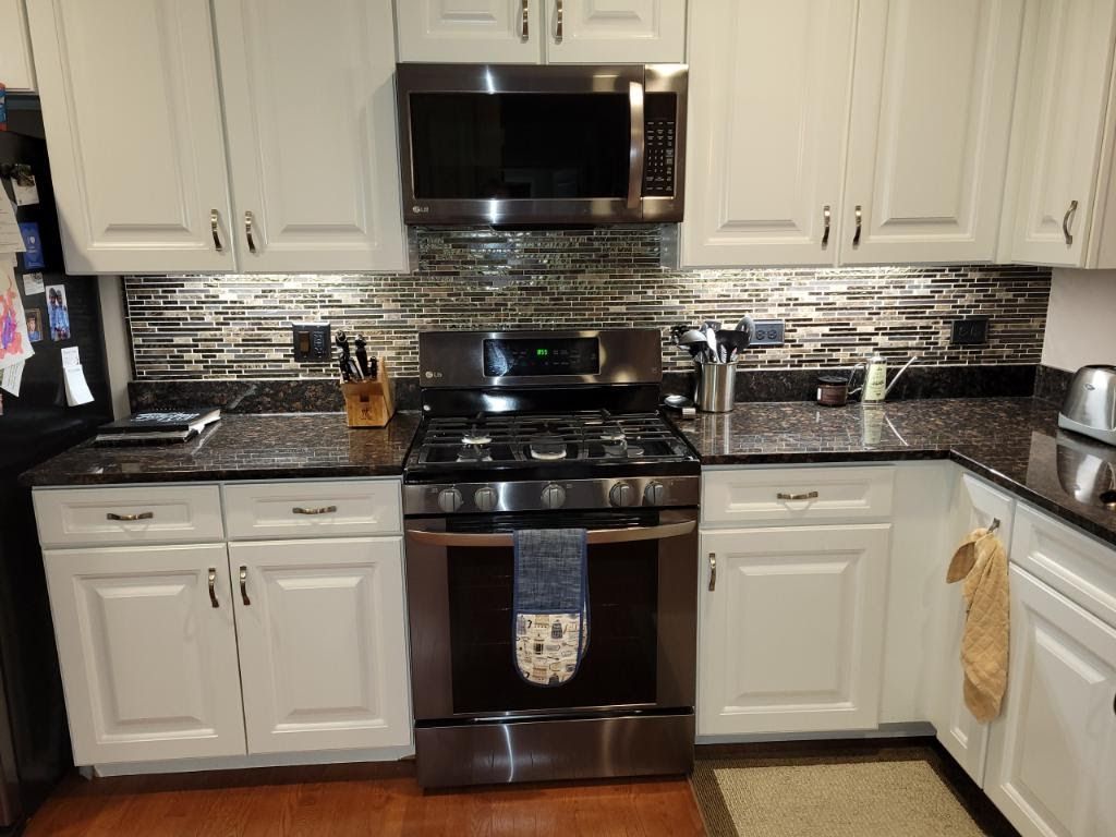 White kitchen with stainless steel stove, microwave, and dishwasher, dark backsplash, and black countertop