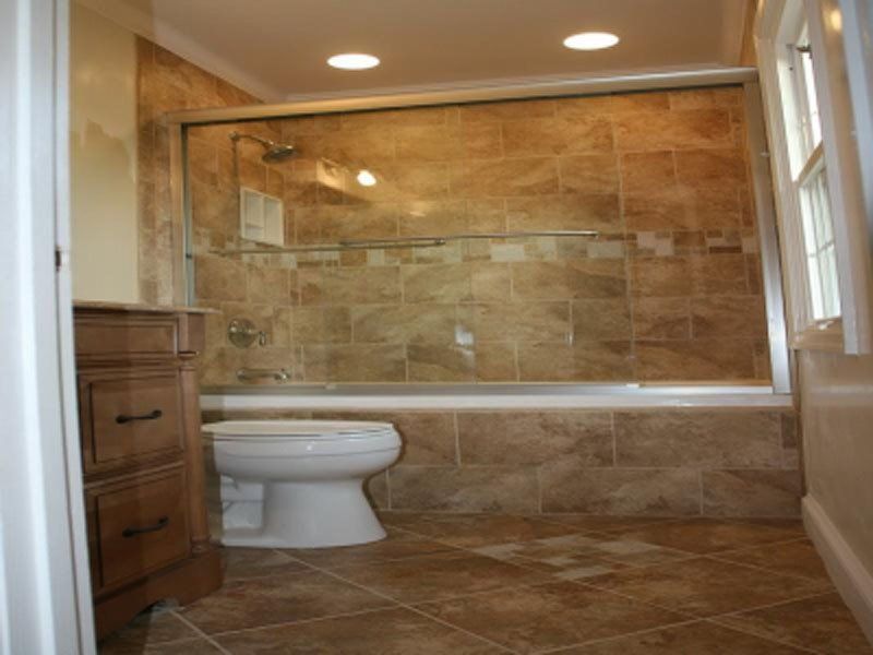 Small beige-tiled bathroom with a toilet, vanity, and glass-enclosed shower area