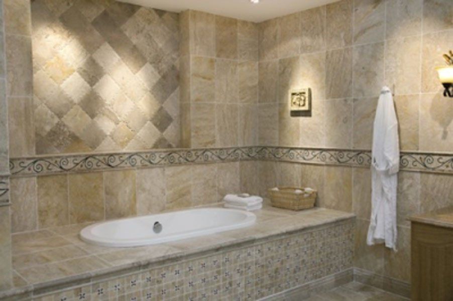 Beige tiled bathroom with built-in bathtub, decorative wall tiles, towel, and basket of towels