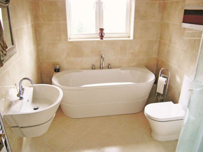 Modern beige bathroom with bathtub, toilet, sink, and a window above the tub