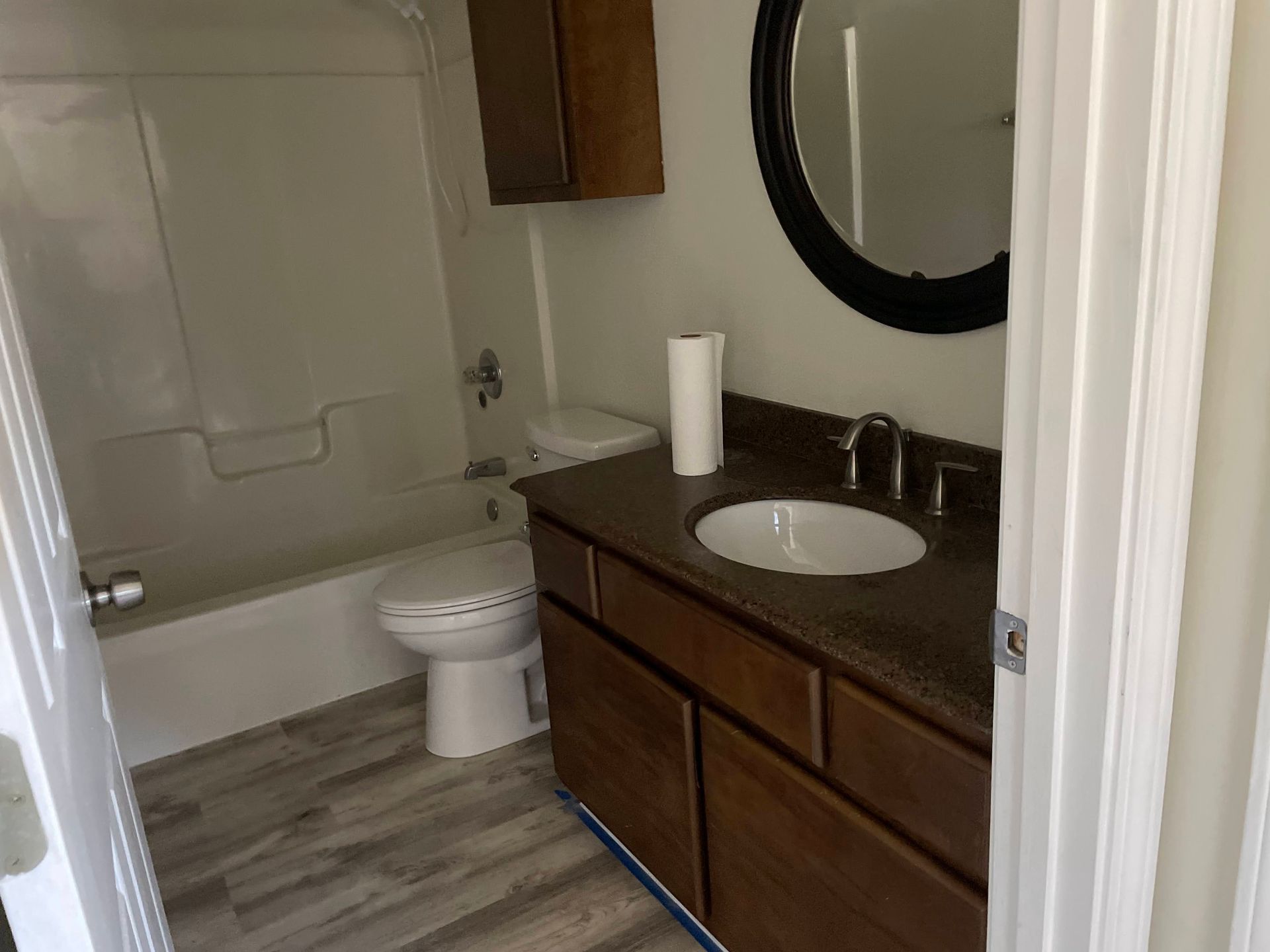 Bathroom with toilet, tub, and dark vanity with sink and round mirror