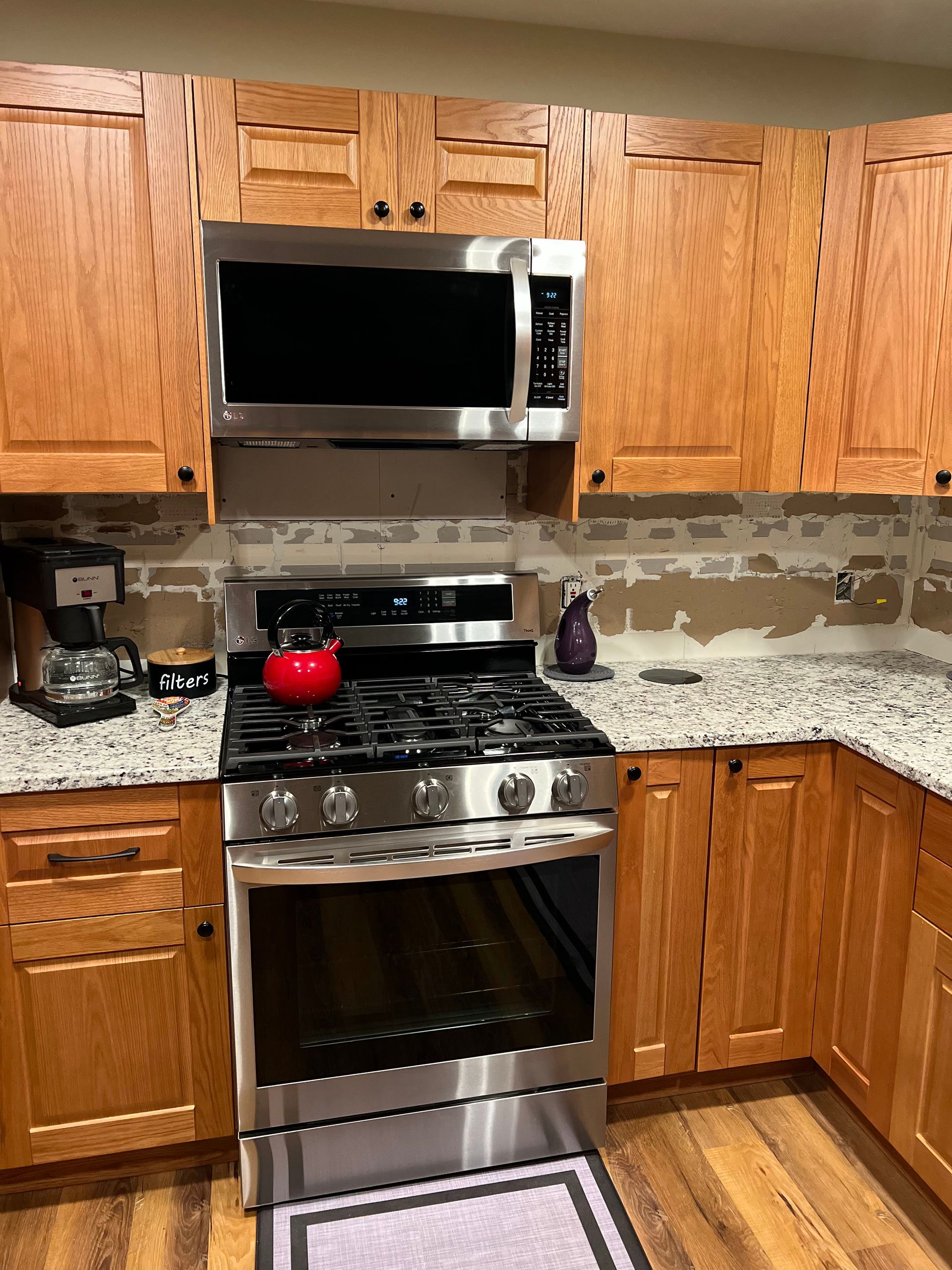 Kitchen with wooden cabinets, stainless steel stove and microwave, granite countertops, and a coffee maker.