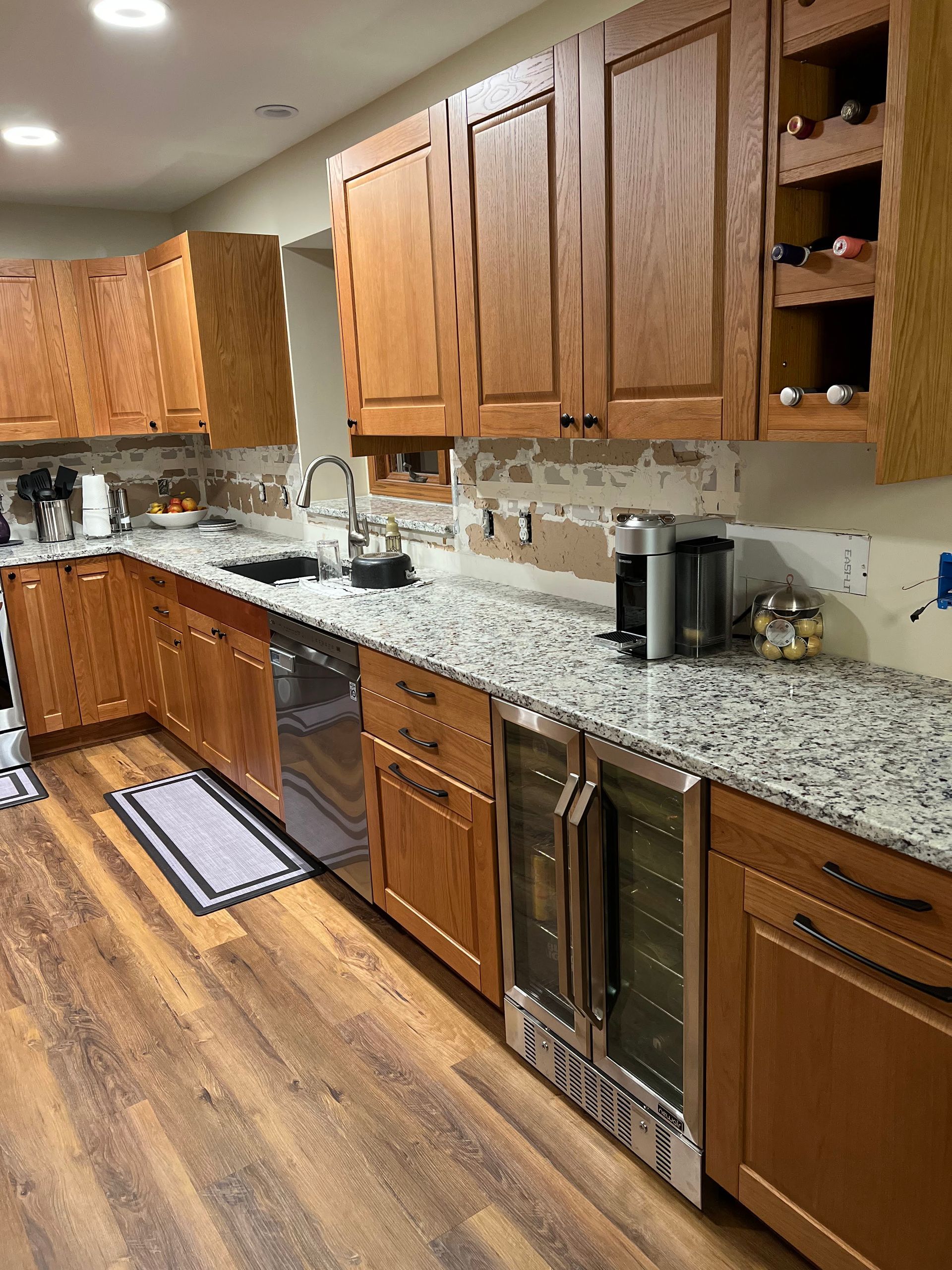 Wooden kitchen with granite counters, sink, dishwasher, coffee maker, and wood flooring.
