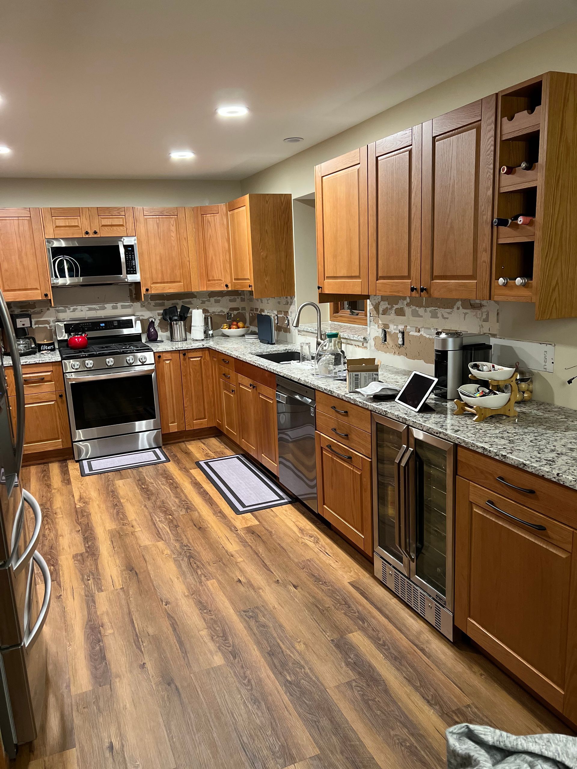 Wooden kitchen with stainless appliances, tan cabinets, and a long counter along the right wall.