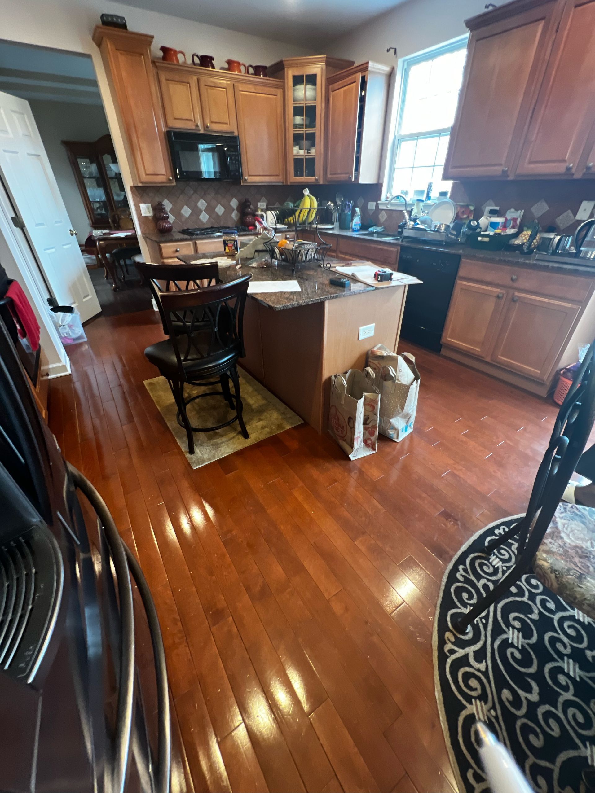 Bright kitchen with wooden cabinets, center island, and hardwood floors; chair and bags near the counter.
