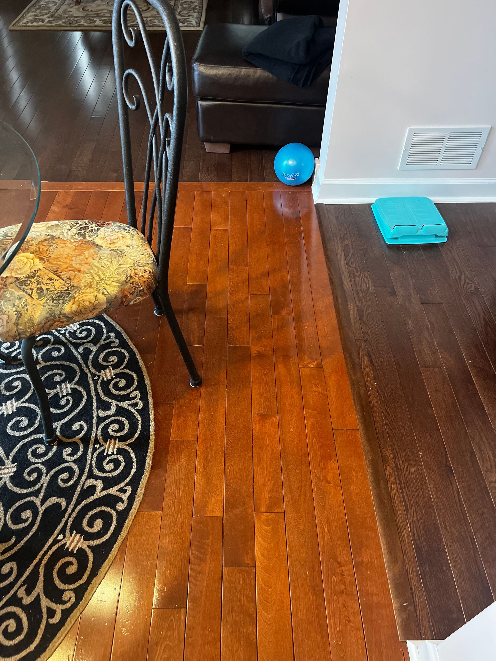 Living room with wooden floor, dining chair, blue ball, and teal folder near a black couch