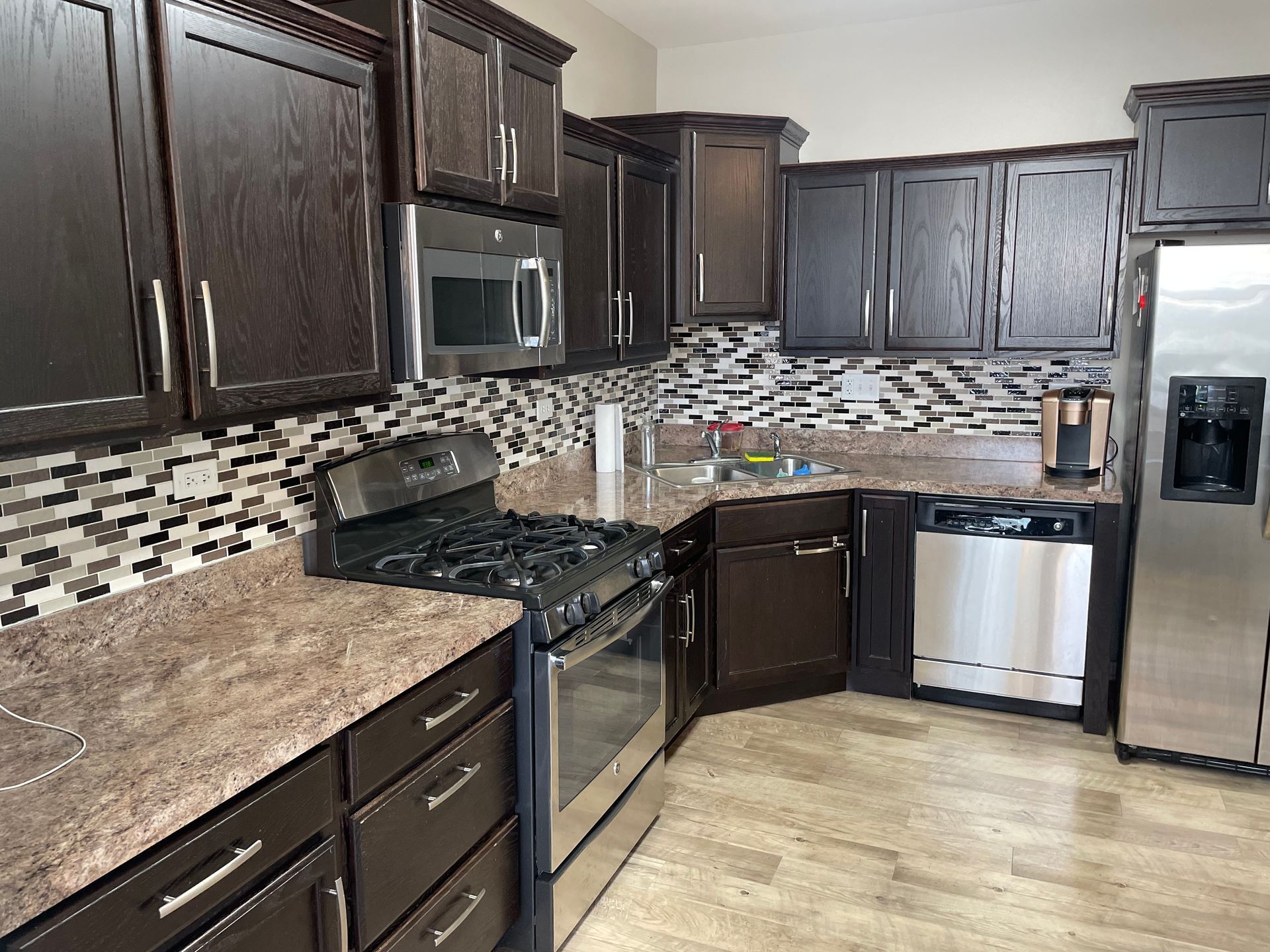 Modern kitchen with dark wood cabinets, stainless steel appliances, and a beige countertop.