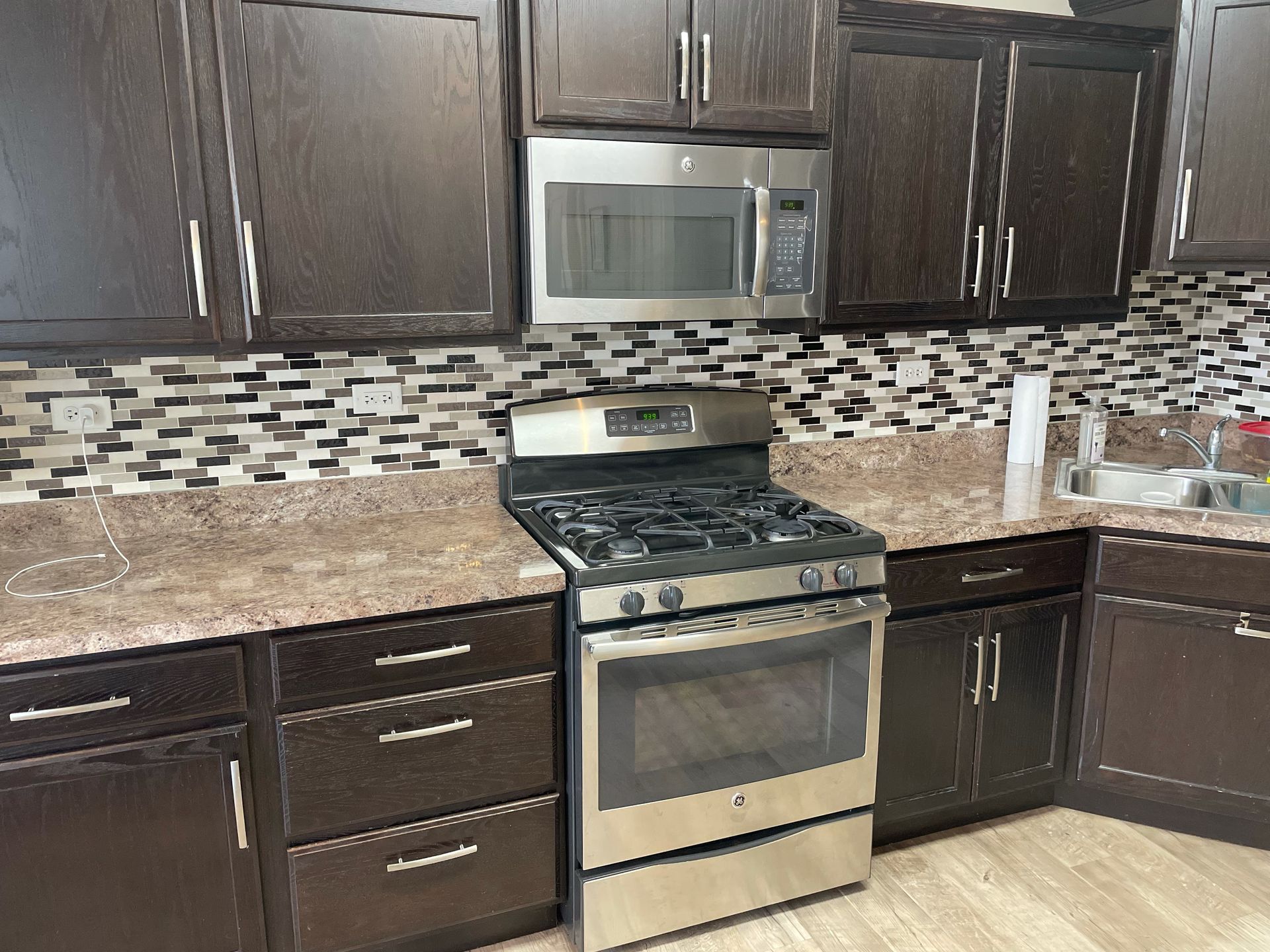 Modern kitchen with dark wood cabinets, stainless steel stove and microwave, and mosaic tile backsplash