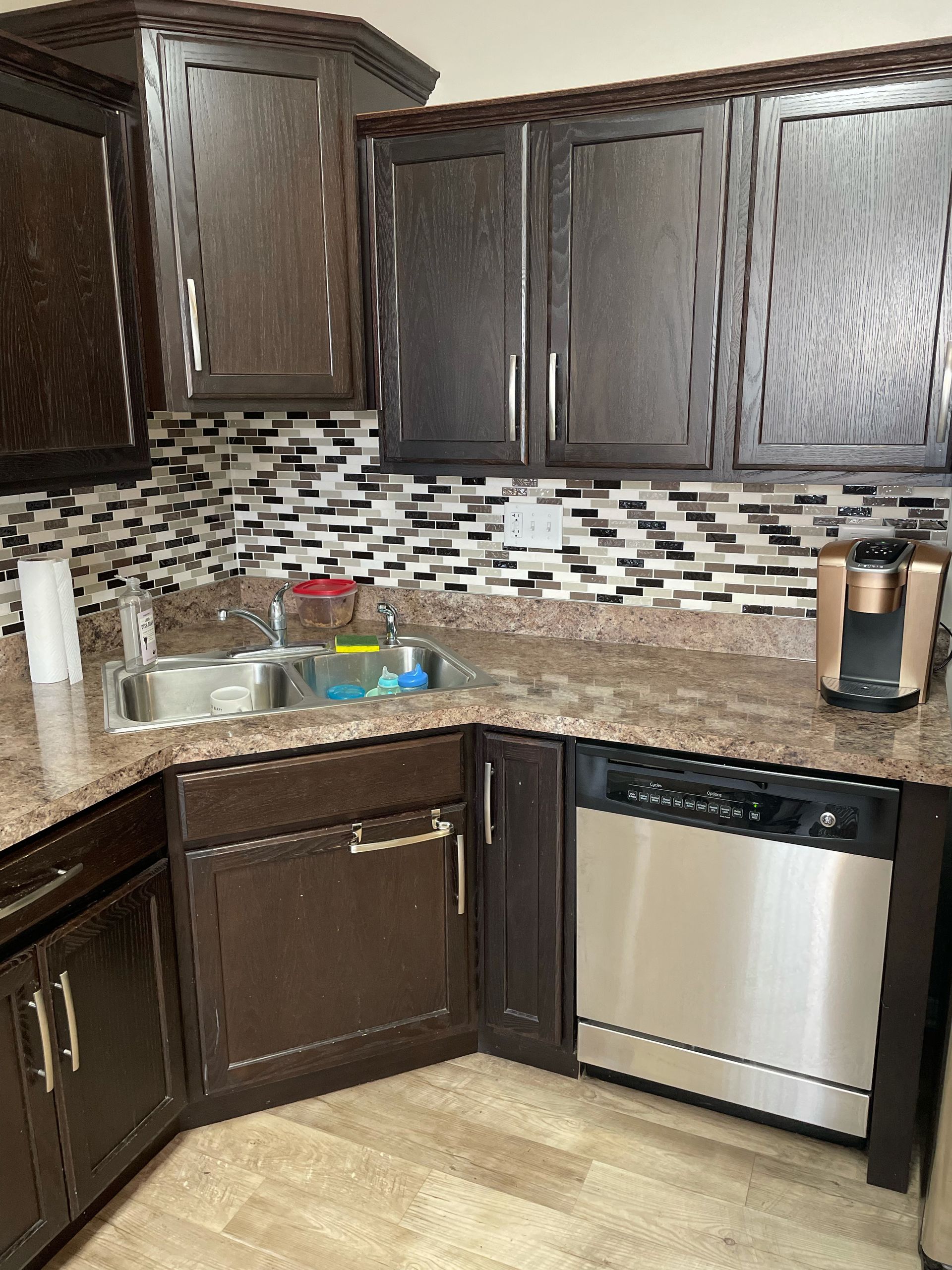 Dark wood kitchen cabinets, granite counters, mosaic backsplash, sink, and stainless dishwasher.