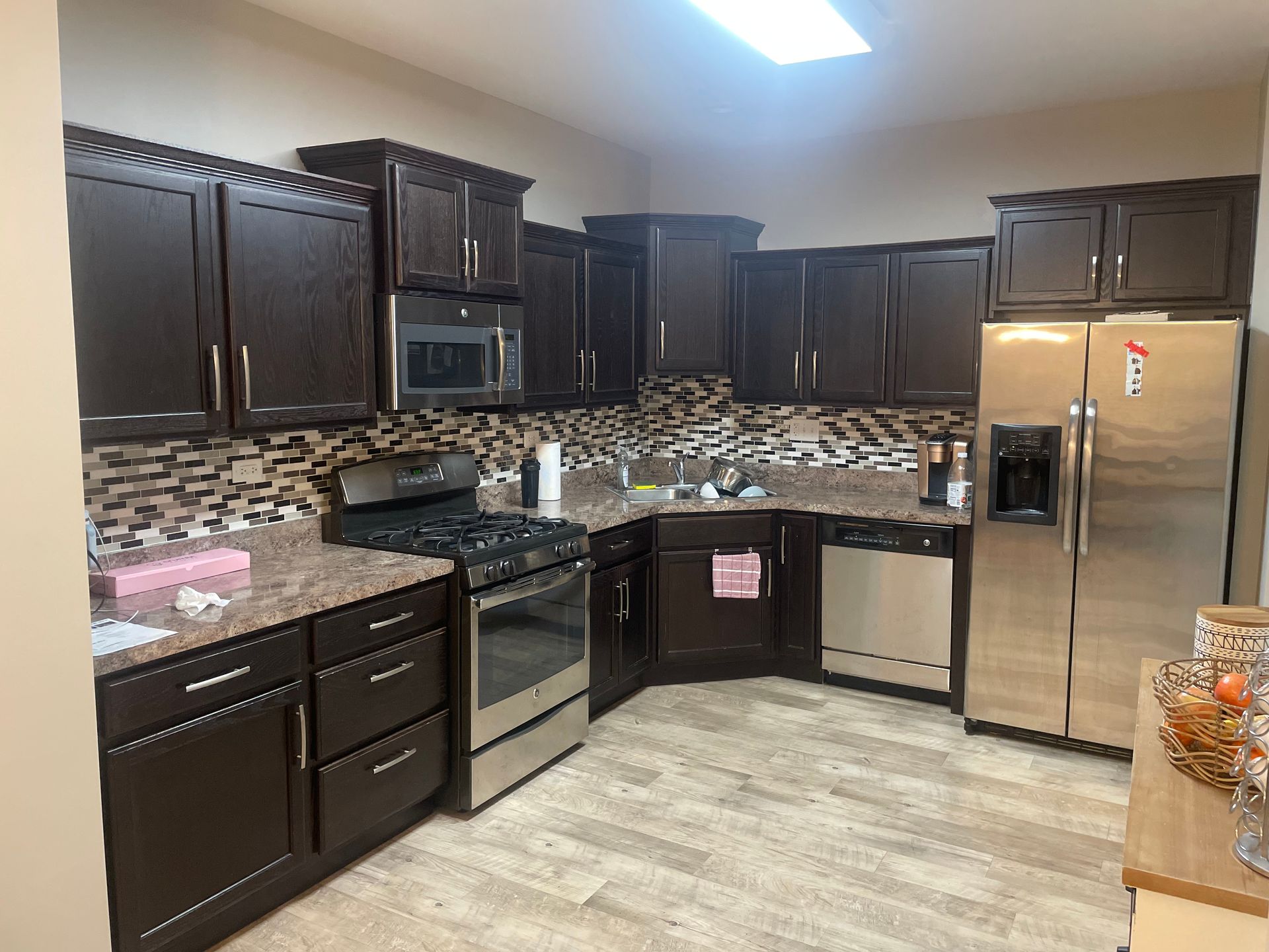 Dark kitchen with black cabinets, stainless appliances, tan backsplash, and light tile floor.