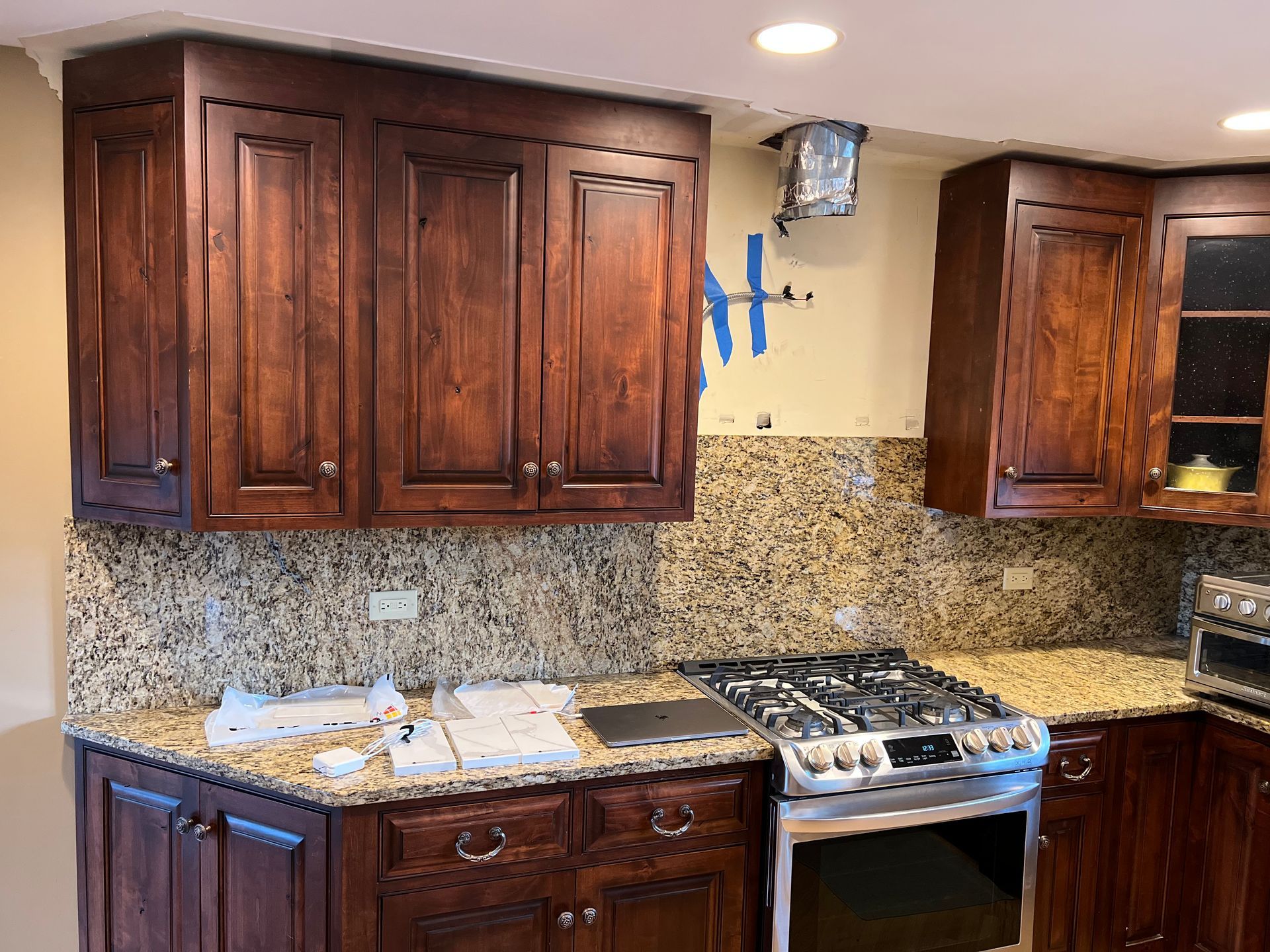 Kitchen with dark wood cabinets, granite countertops, and stainless steel stove under warm recessed lighting