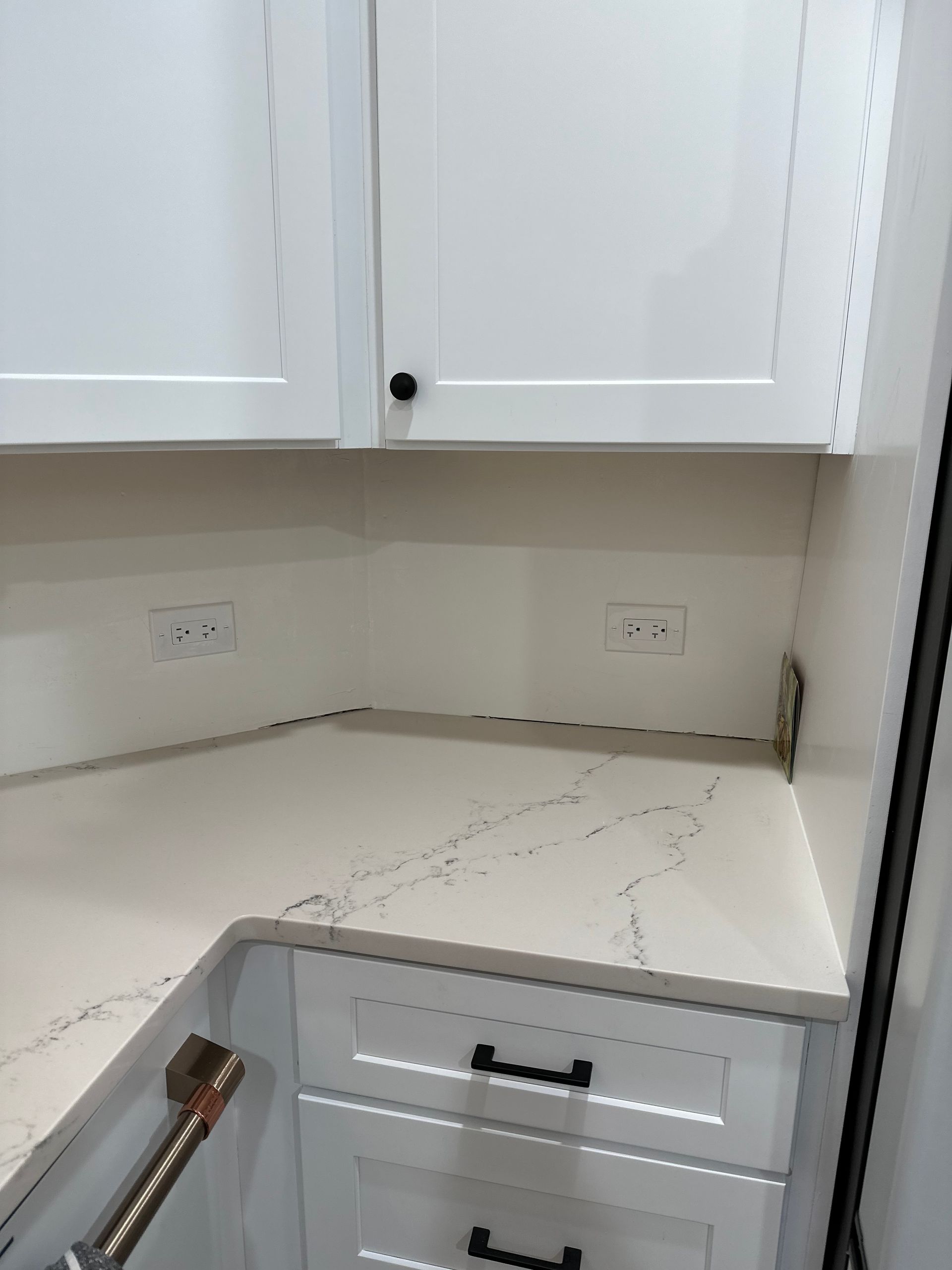 White kitchen corner with marble countertop, white cabinets, and an open drawer under the counter.