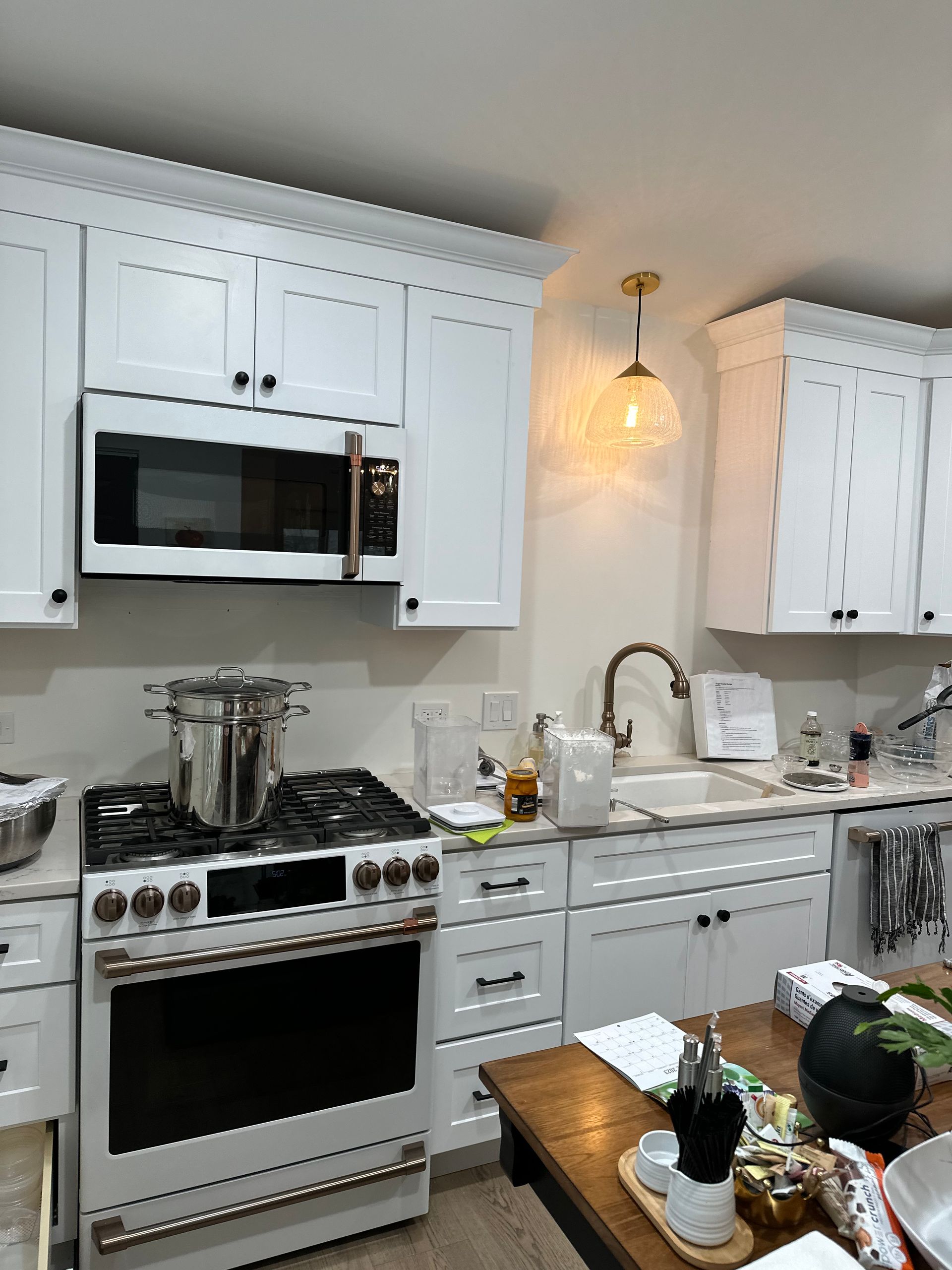 Bright white kitchen with stove, microwave, sink, pendant light, and a table with fruit in the foreground