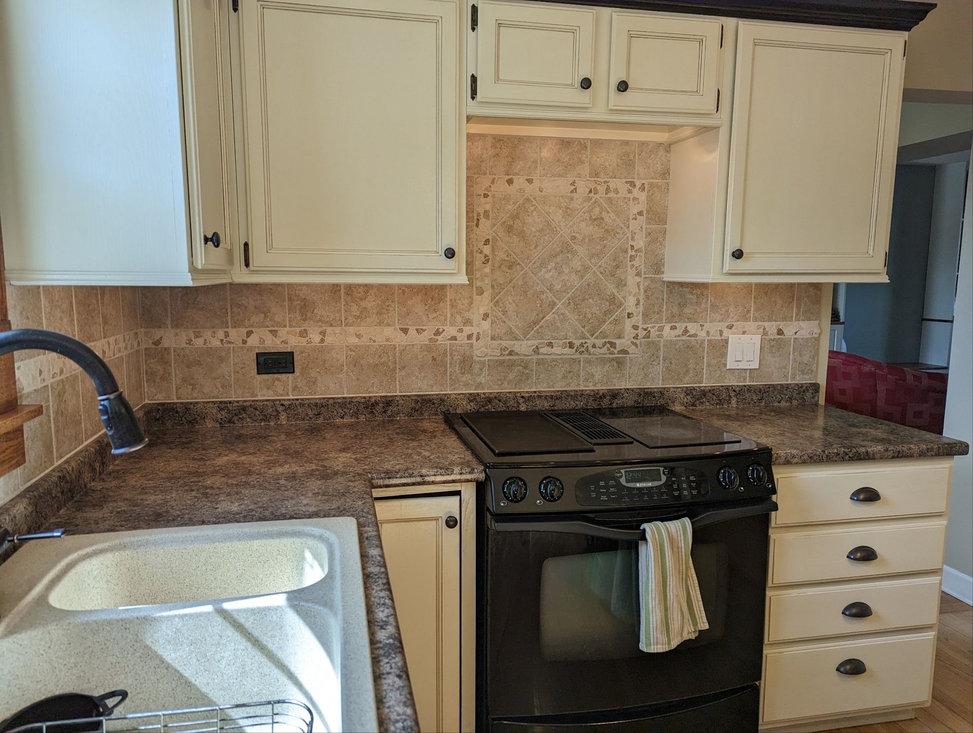 Kitchen with white cabinets, granite countertops, tiled backsplash, and black stove beside a sink.
