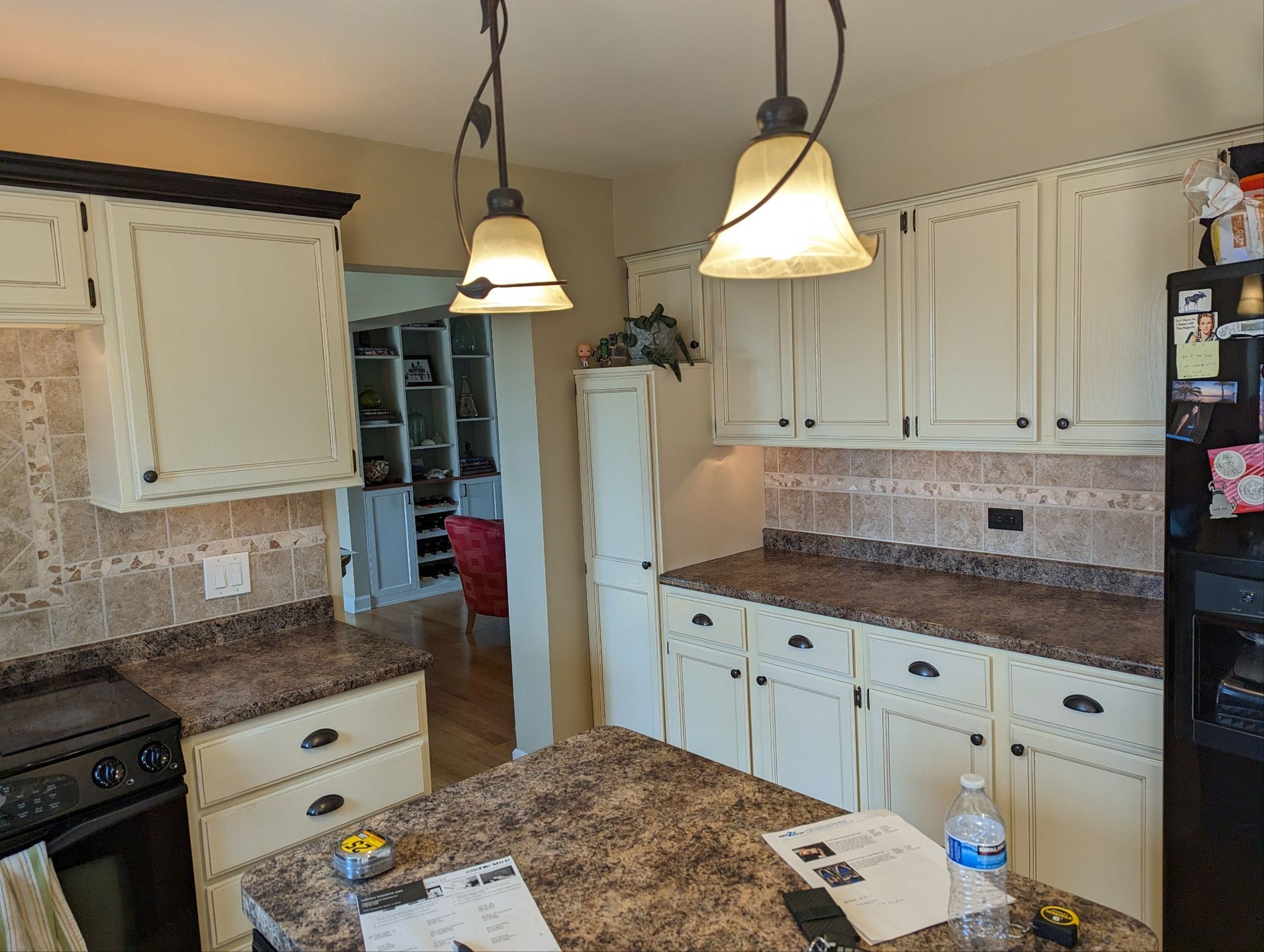 Kitchen with white cabinets, granite counters, hanging pendant lights, and a refrigerator by the doorway