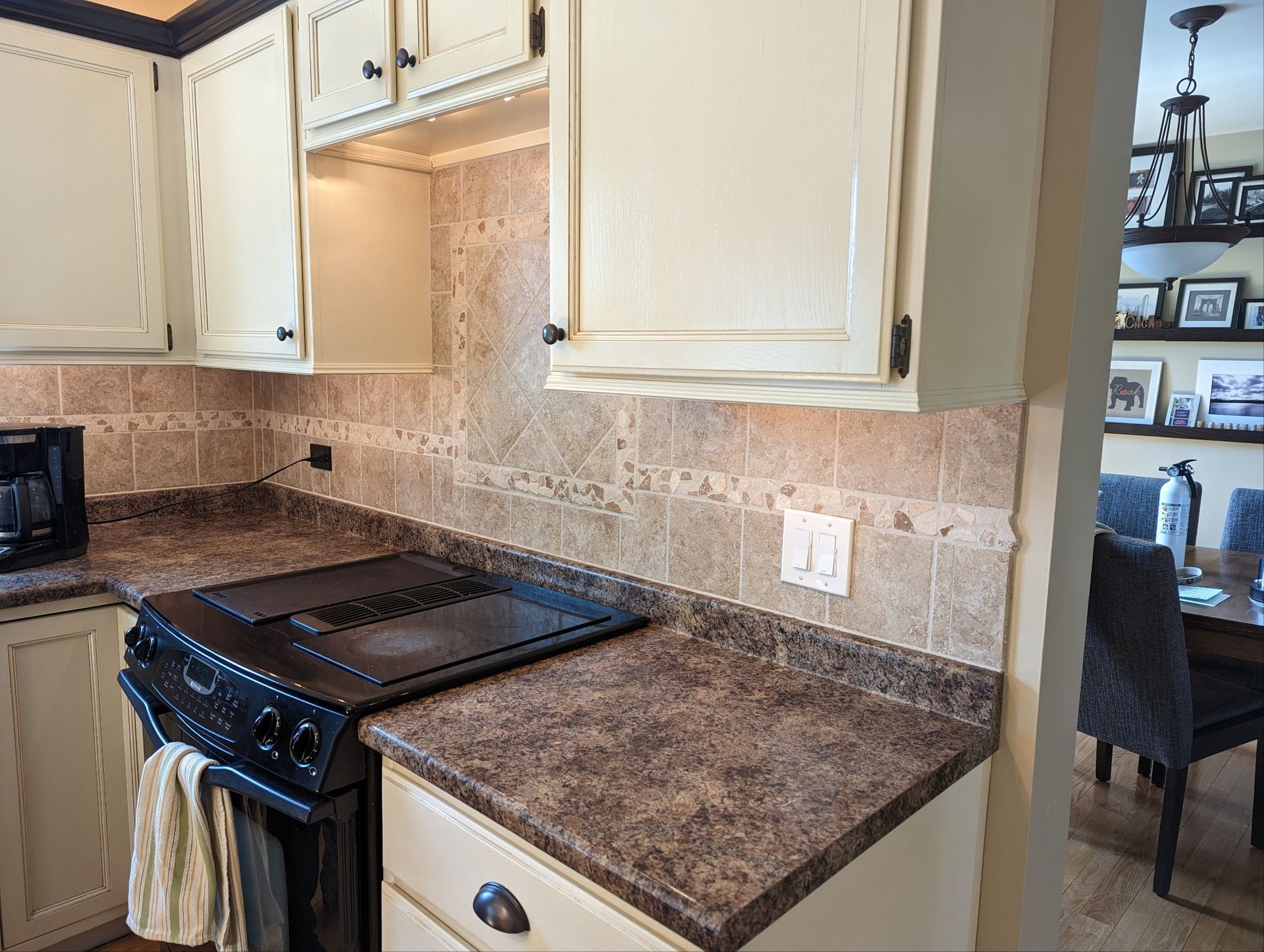 Kitchen with beige cabinets, brown countertops, and a black stove against a tile backsplash.