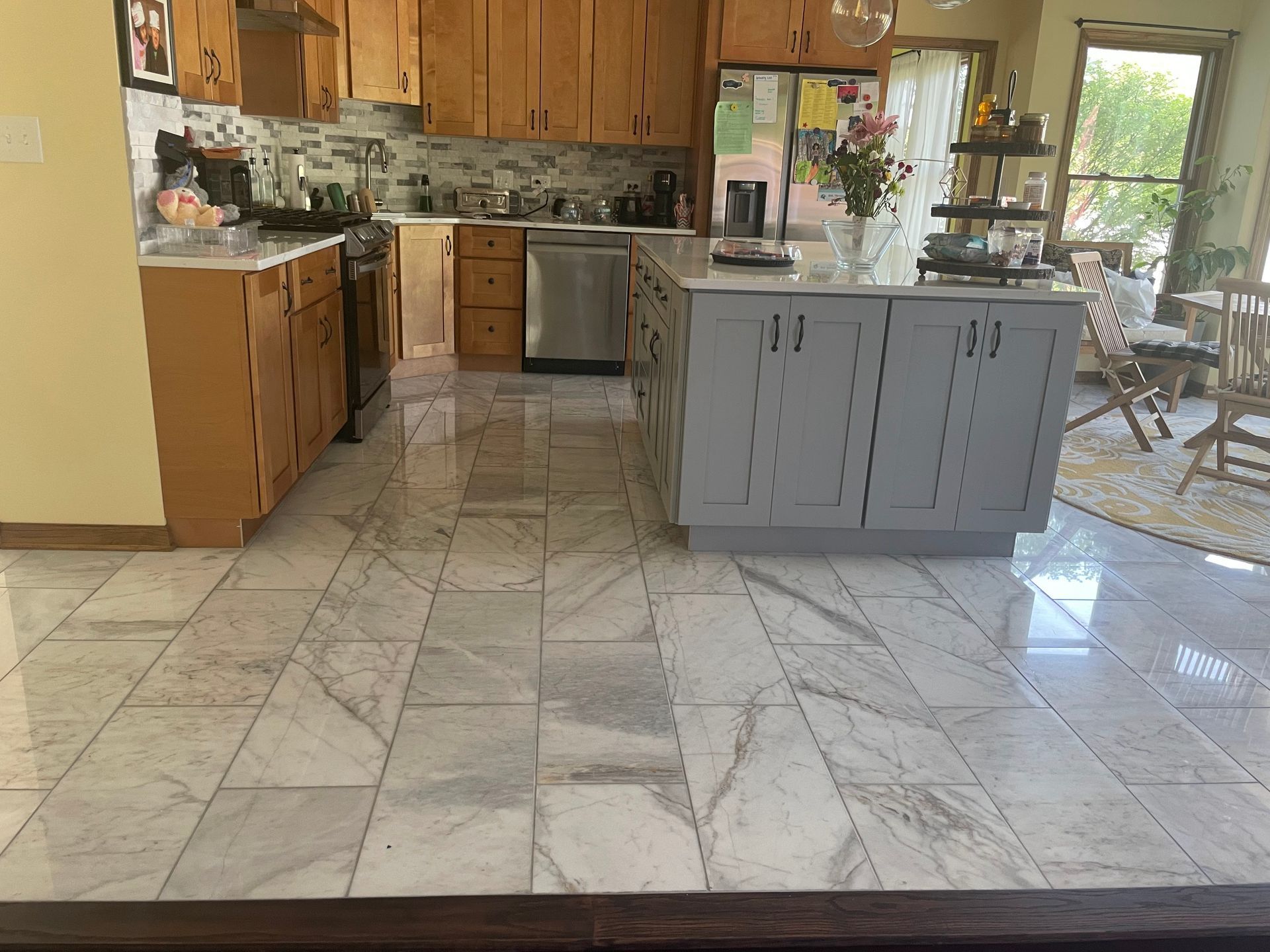 Bright kitchen with marble tile floor, wood cabinets, stainless appliances, and a gray island.