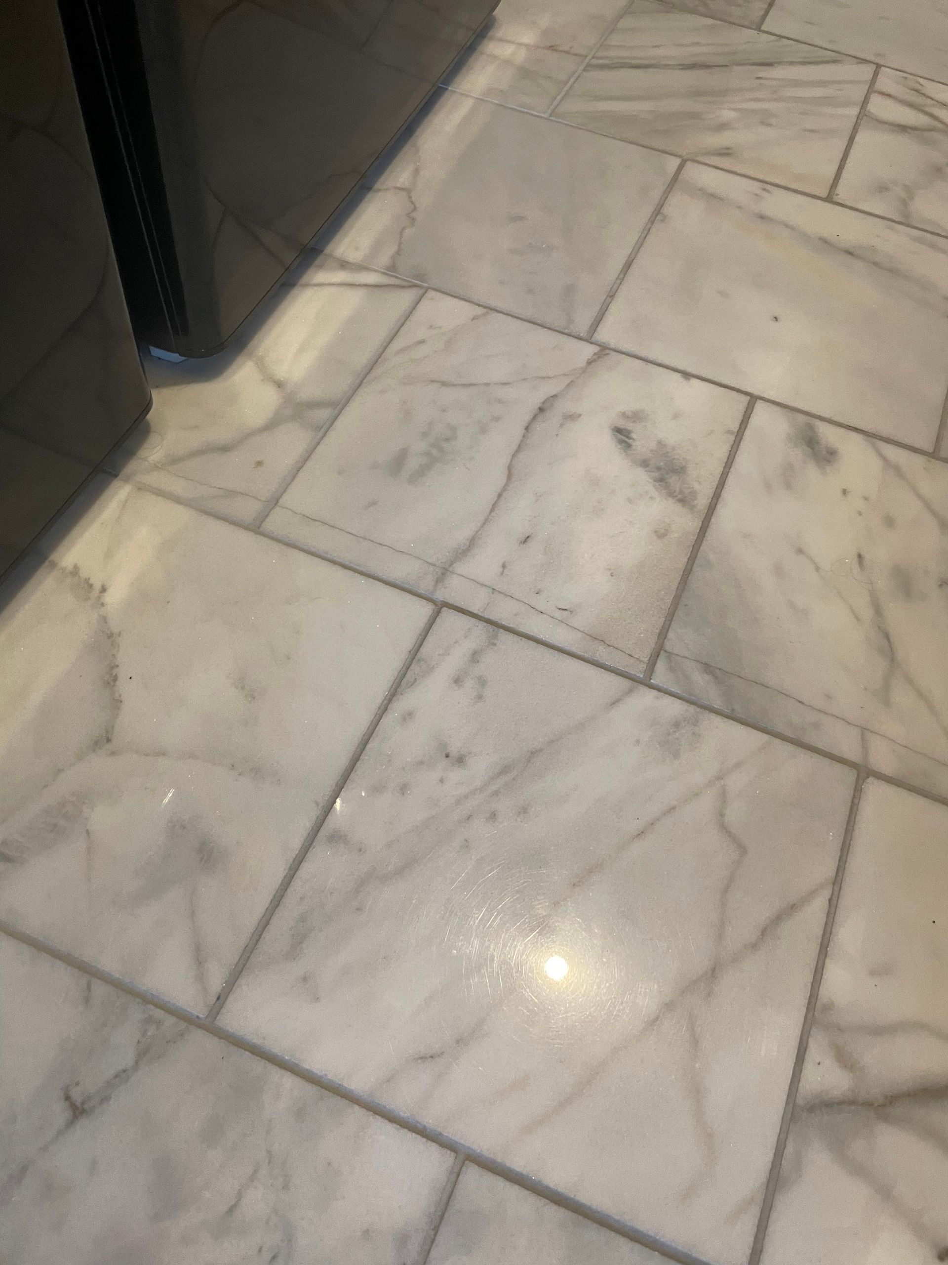 Light gray marble tile floor with dark grout lines, viewed from above beside a dark wall edge.