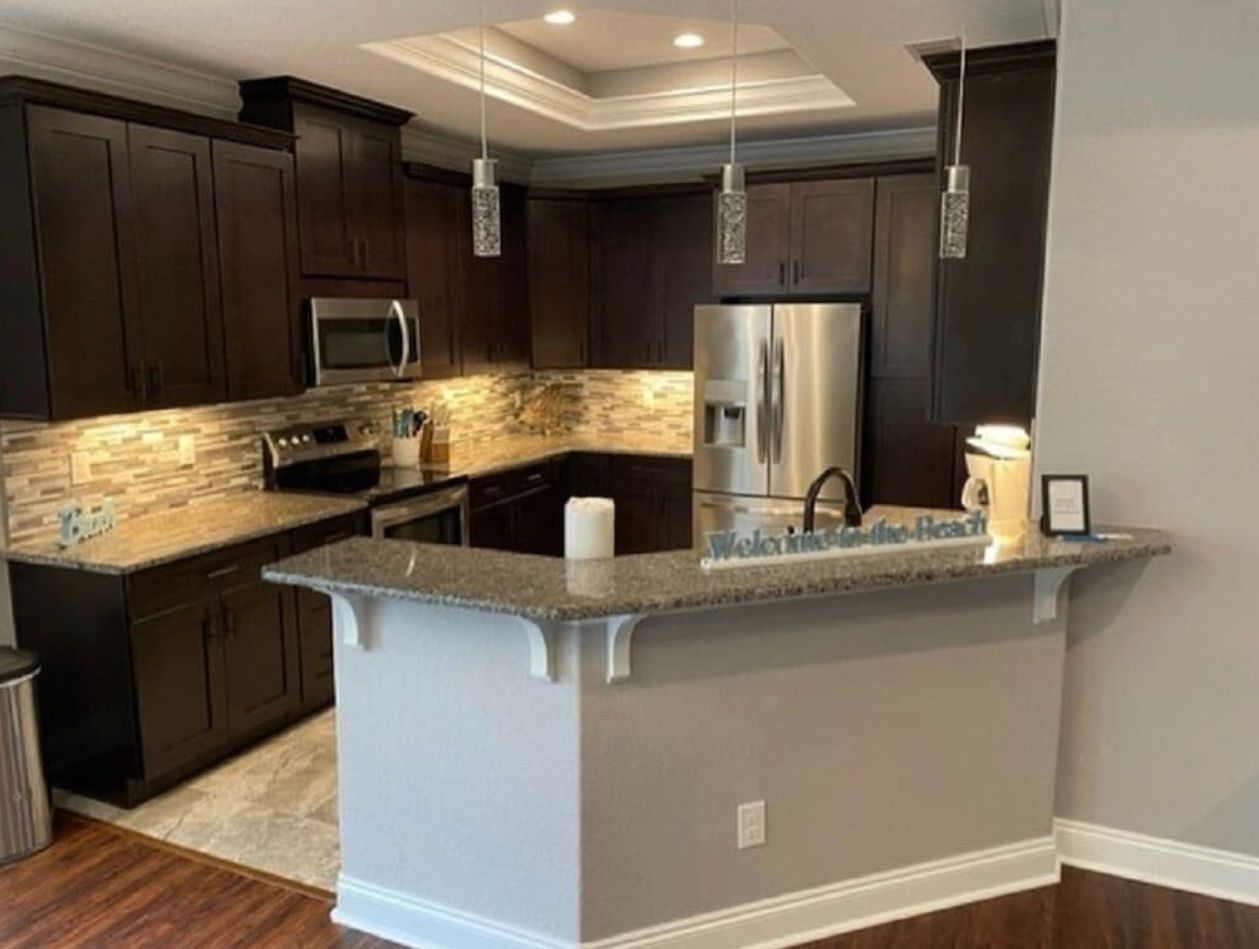 Modern kitchen with dark cabinets, stainless appliances, granite island, and pendant lights
