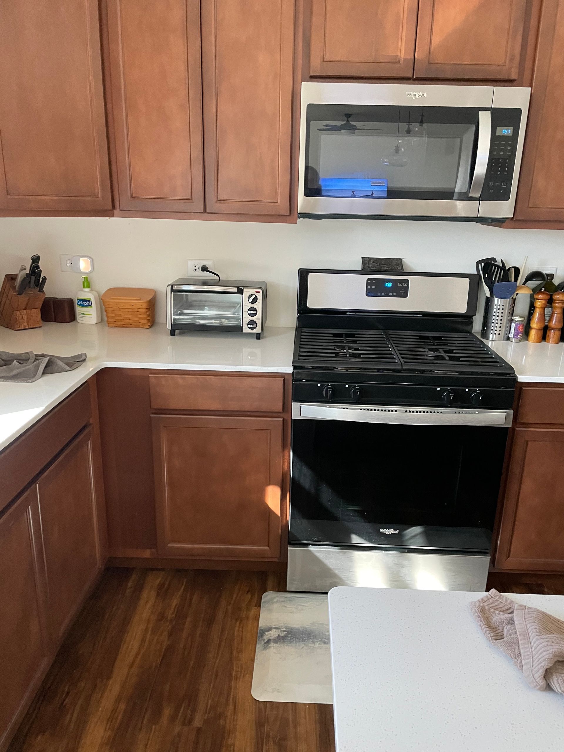 Kitchen with wooden cabinets, stainless steel stove and microwave, toaster on counter, and white table in foreground