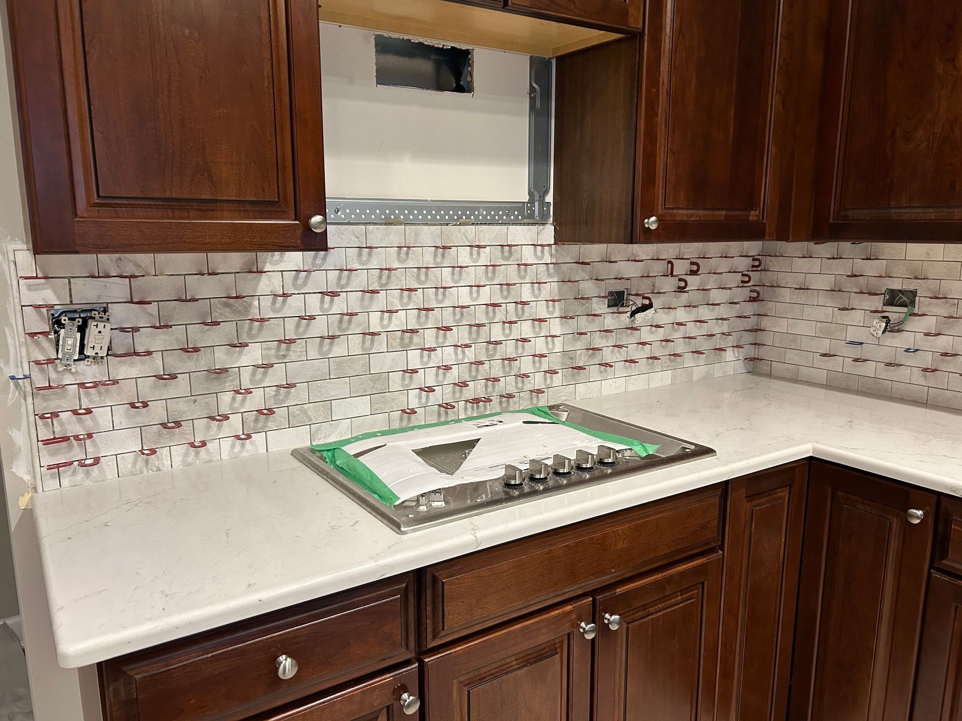 Kitchen with dark wood cabinets, white countertops, and a mosaic tile backsplash around a sink area.