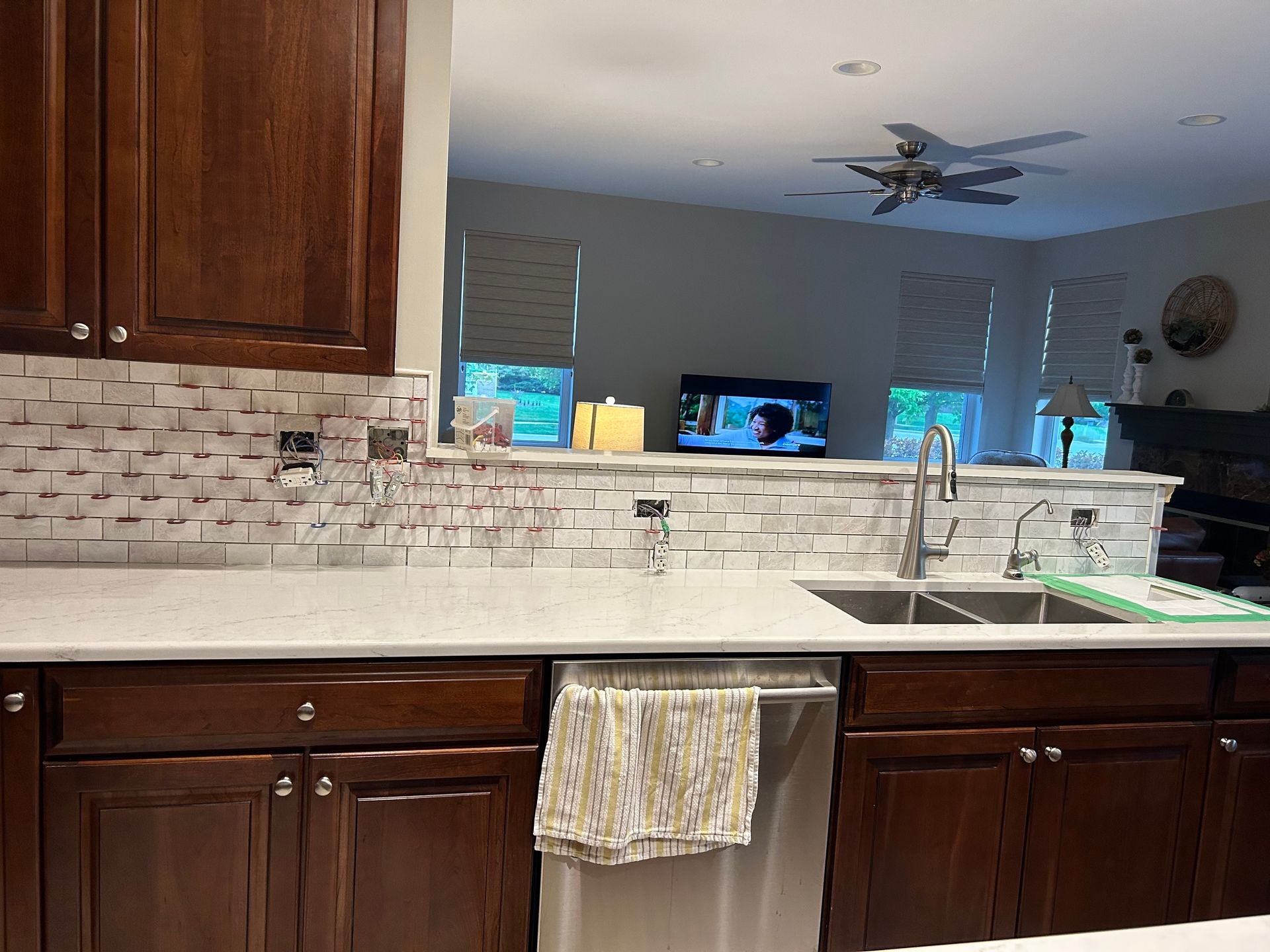 Kitchen with dark wood cabinets, white countertop, tiled backsplash, and view into a living room.