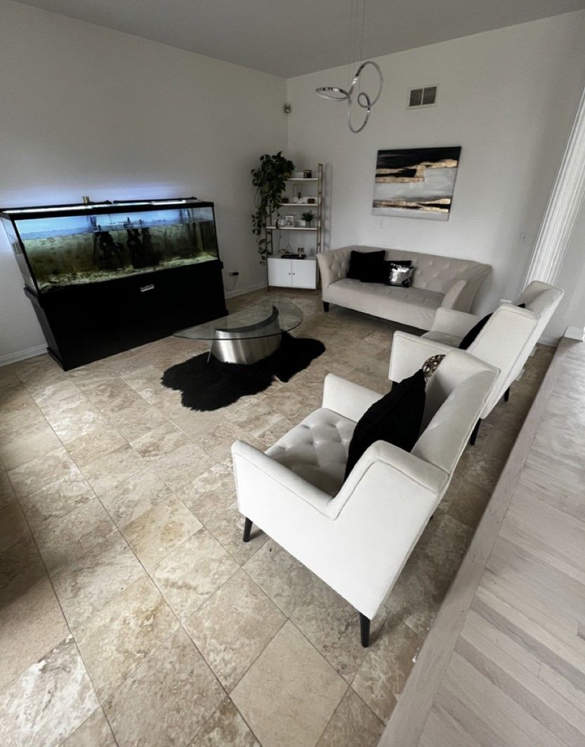 Modern living room with large aquarium, white sofas, black rug, and tiled floor.