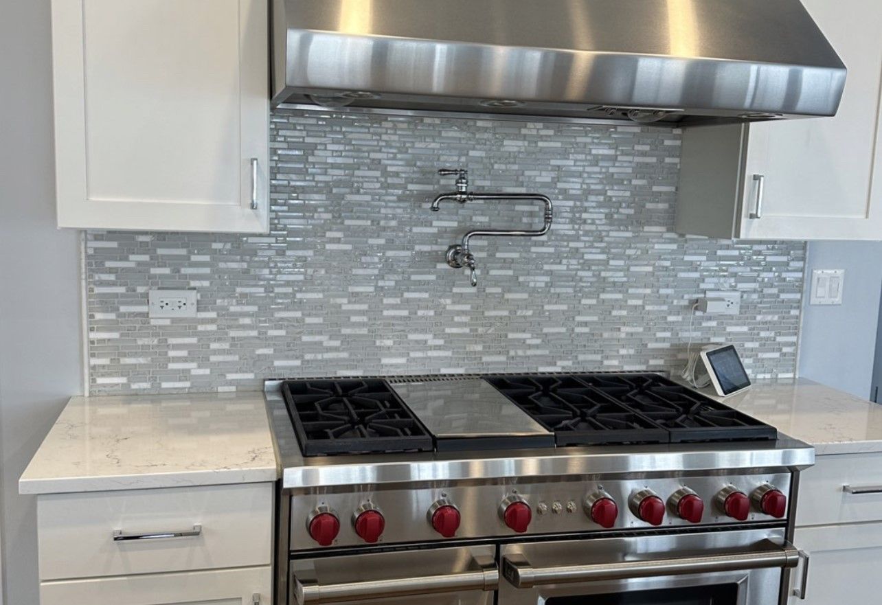 Modern kitchen with stainless steel range, hood, and gray tile backsplash under white cabinets