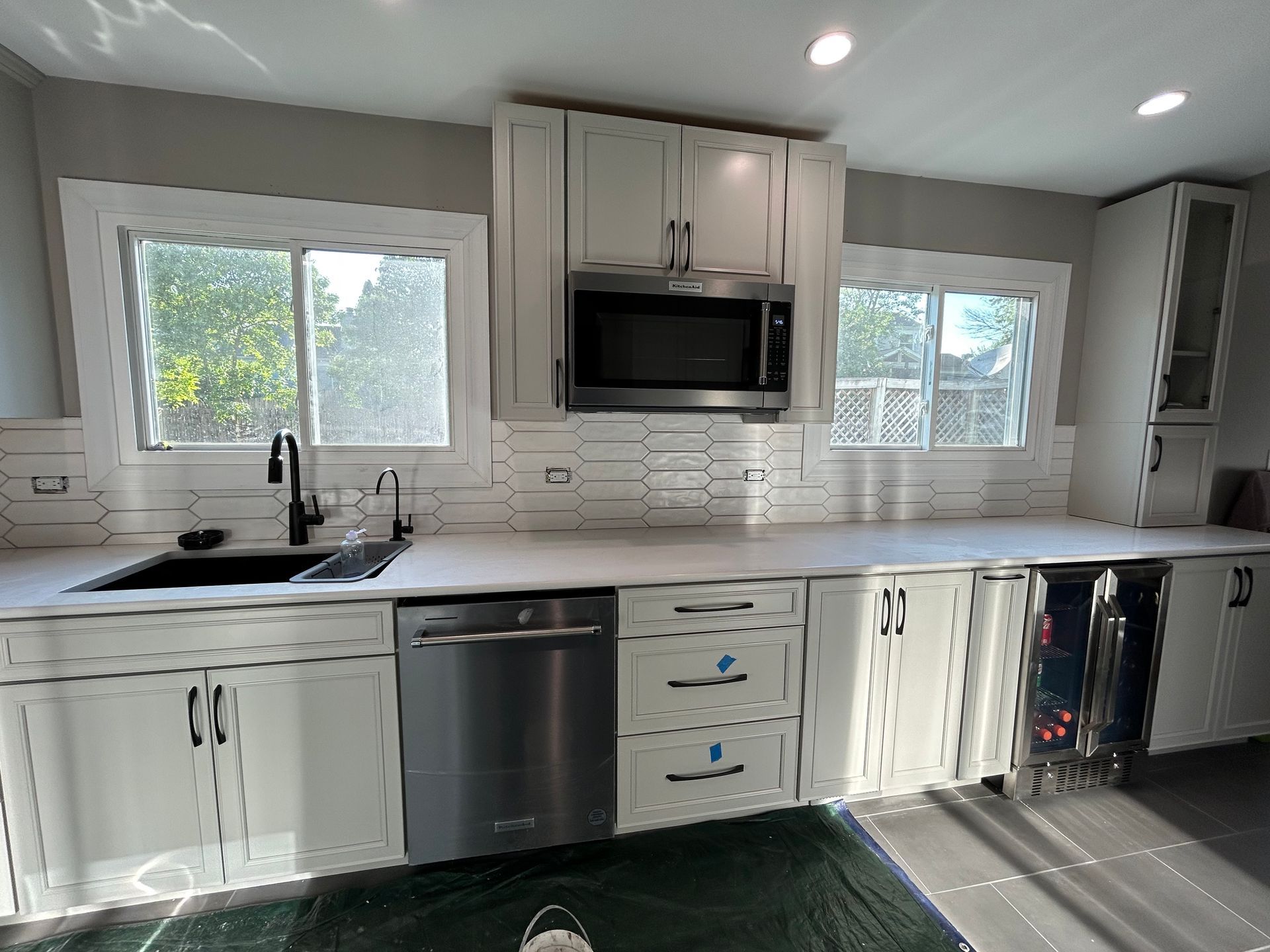 Bright modern kitchen with white cabinets, stainless appliances, and gray countertops by large windows