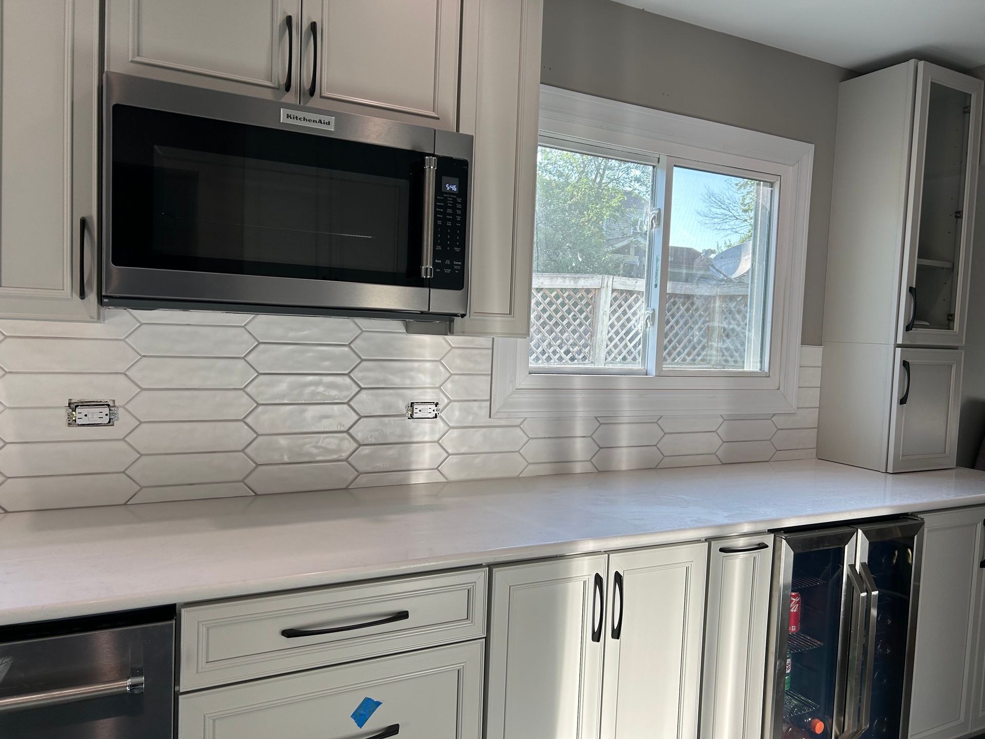 Modern white kitchen with stainless microwave, hex tile backsplash, and a window over the counter