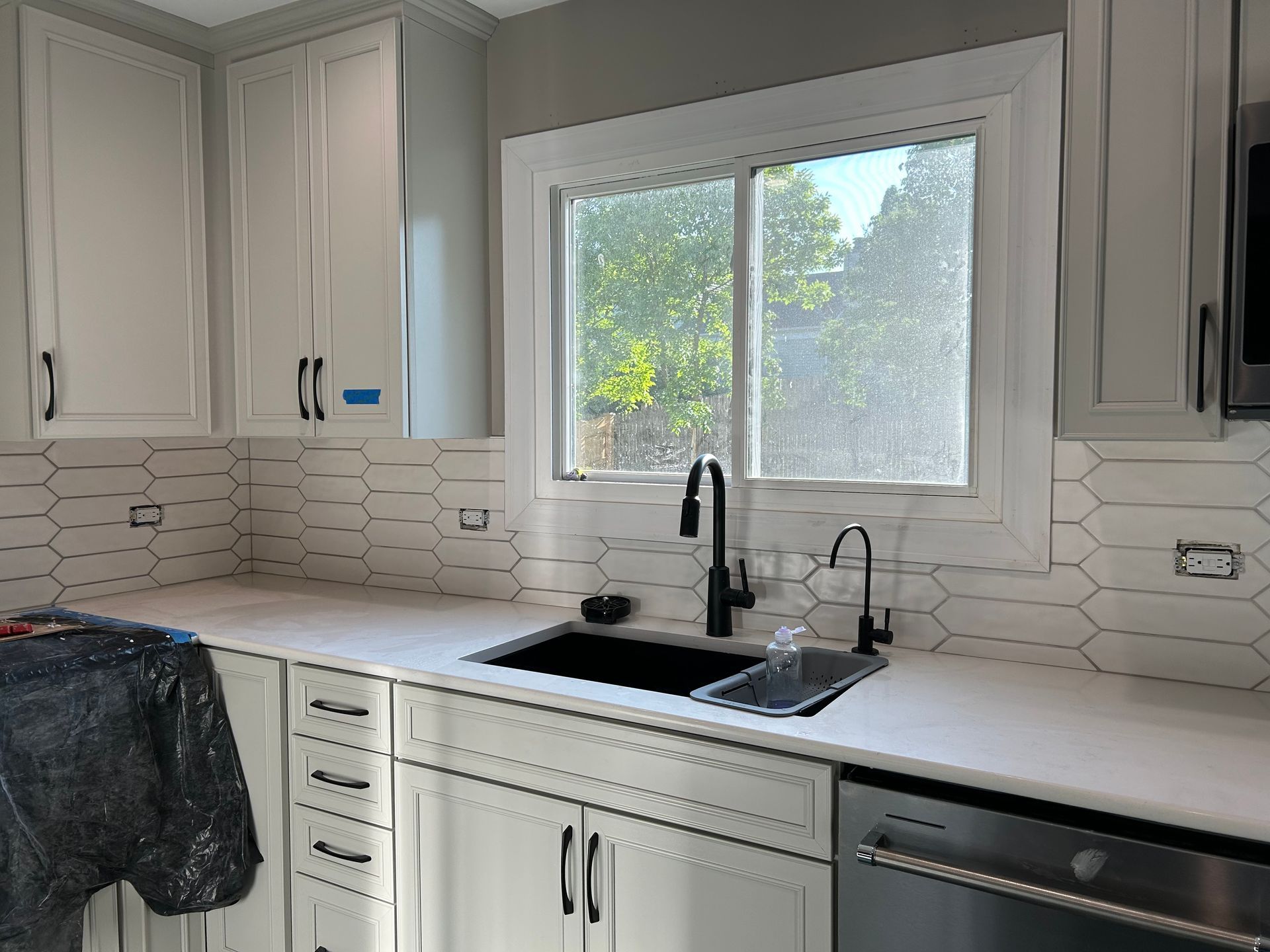 Bright white kitchen with window over sink, black faucet, light tile backsplash, and dishwasher