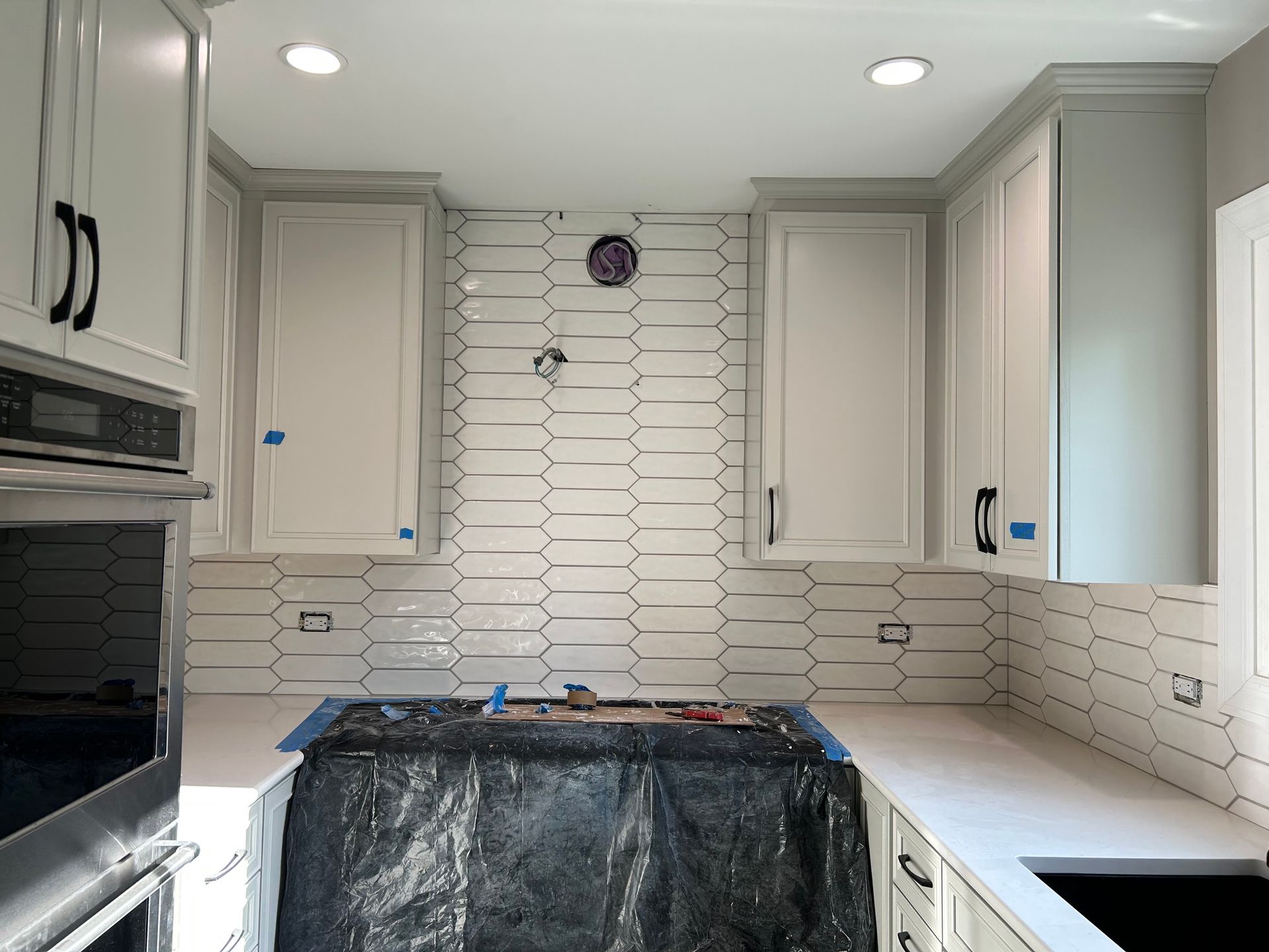 Kitchen under renovation with white cabinets, tiled backsplash, and covered island sink