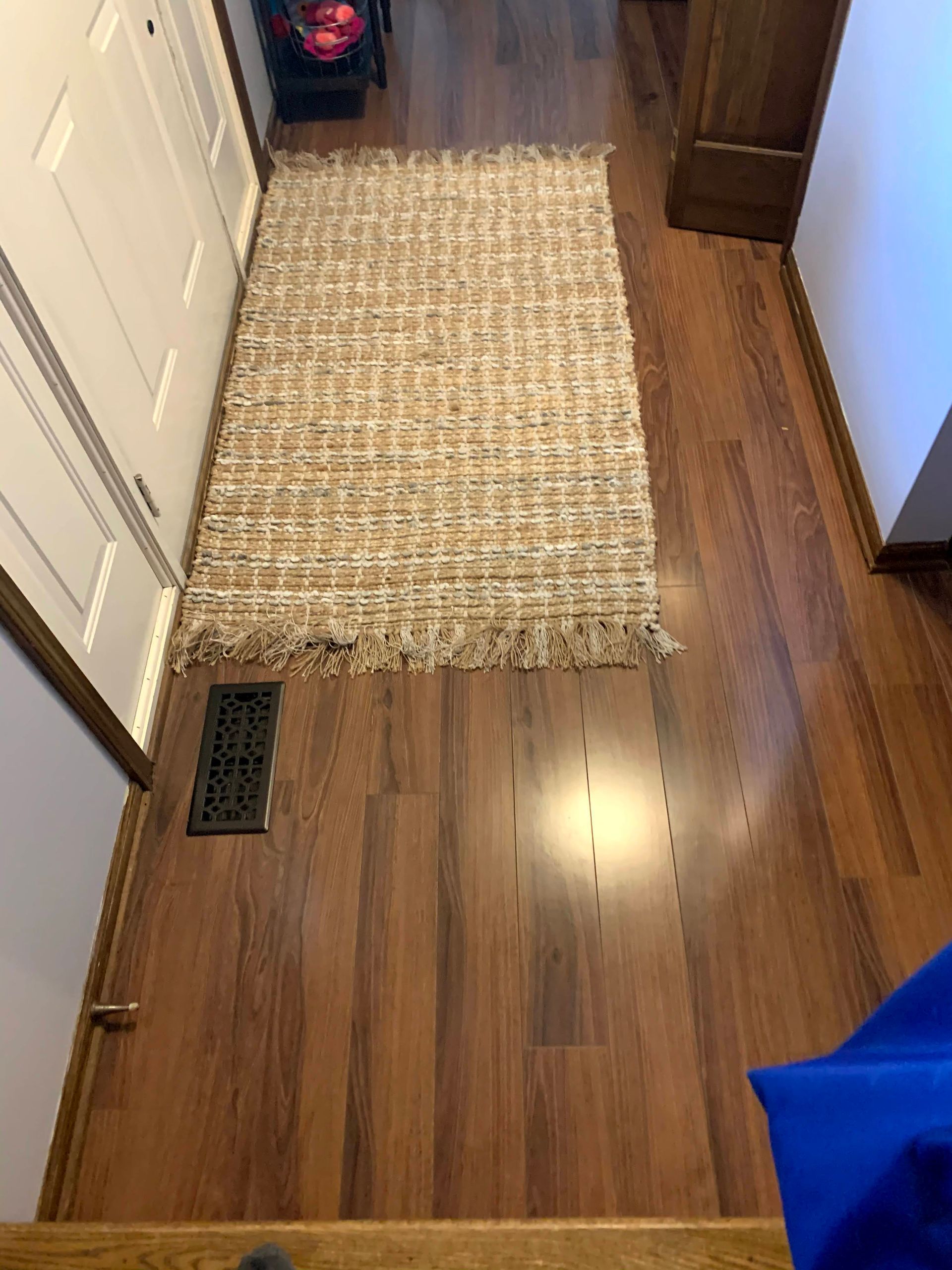 Narrow hallway with hardwood floor, beige runner rug, floor vent, and a dark cabinet at the end.