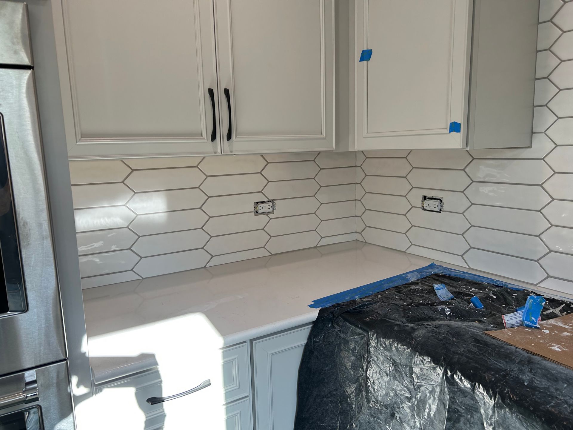 Kitchen with white cabinets, hex tile backsplash, and a countertop under renovation with blue tape and tools.