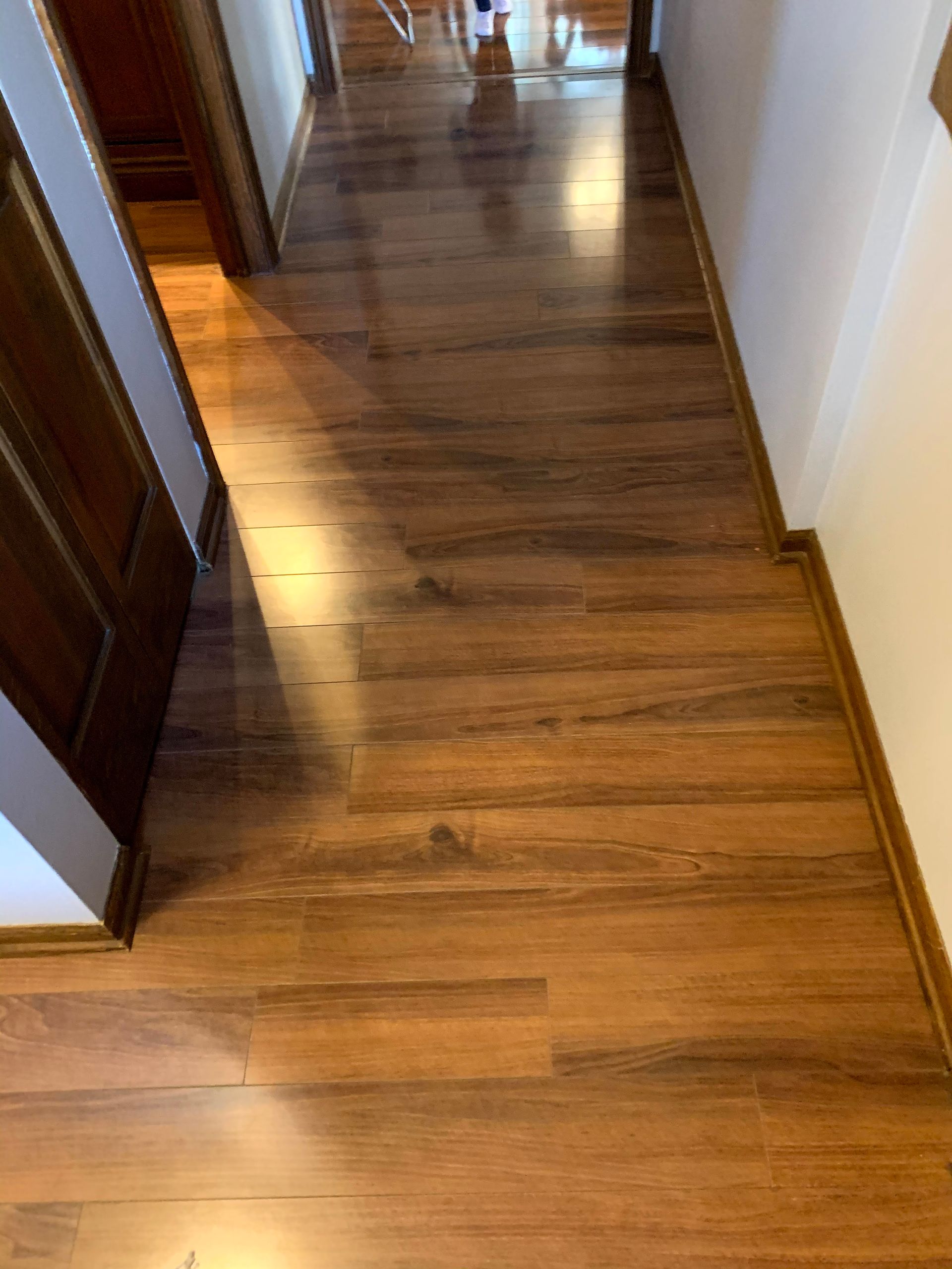 Wooden hallway floor with sunlight reflecting near doorways and white walls